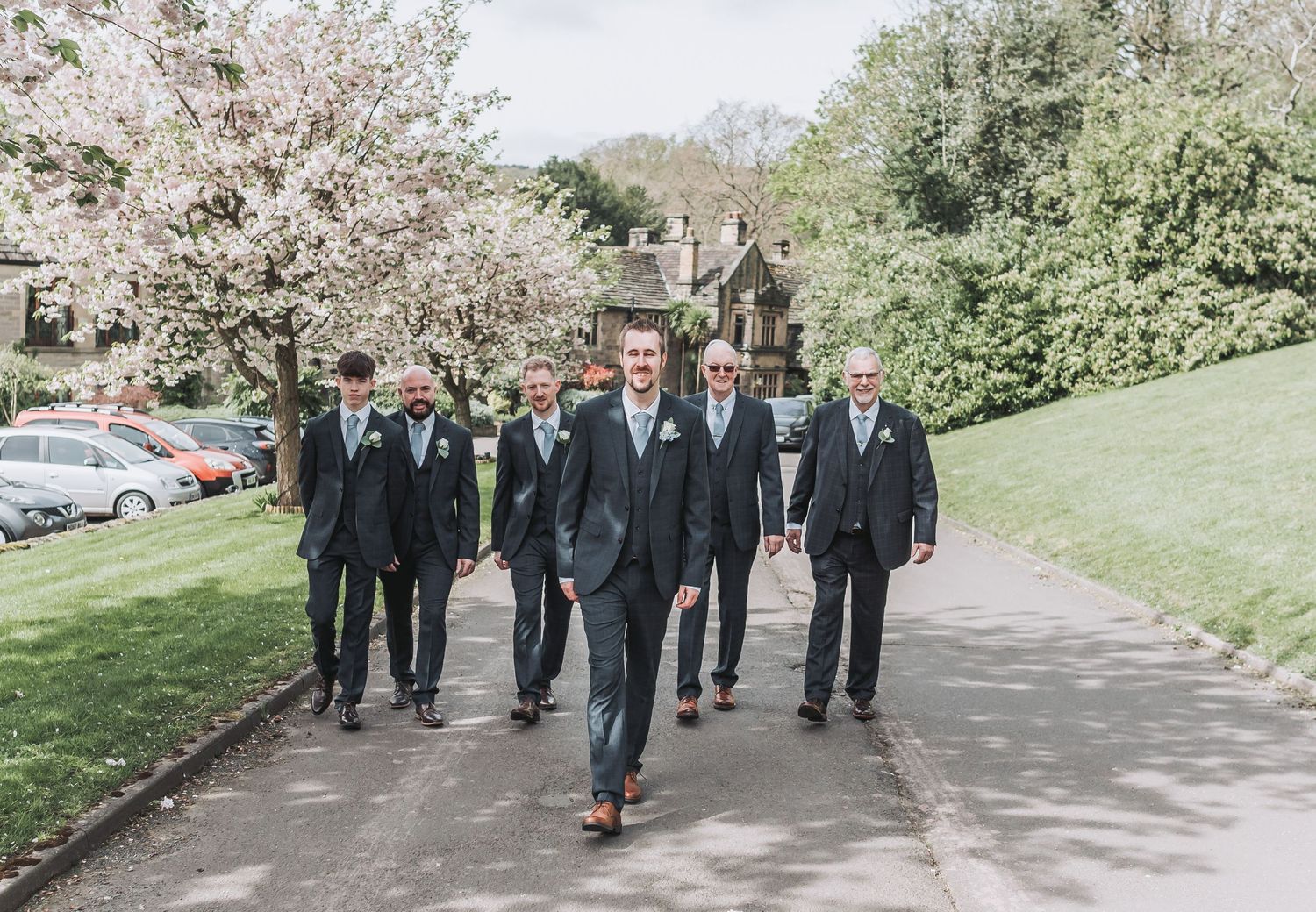 Groomsmen walking together on a spring path with cherry blossoms in bloom.