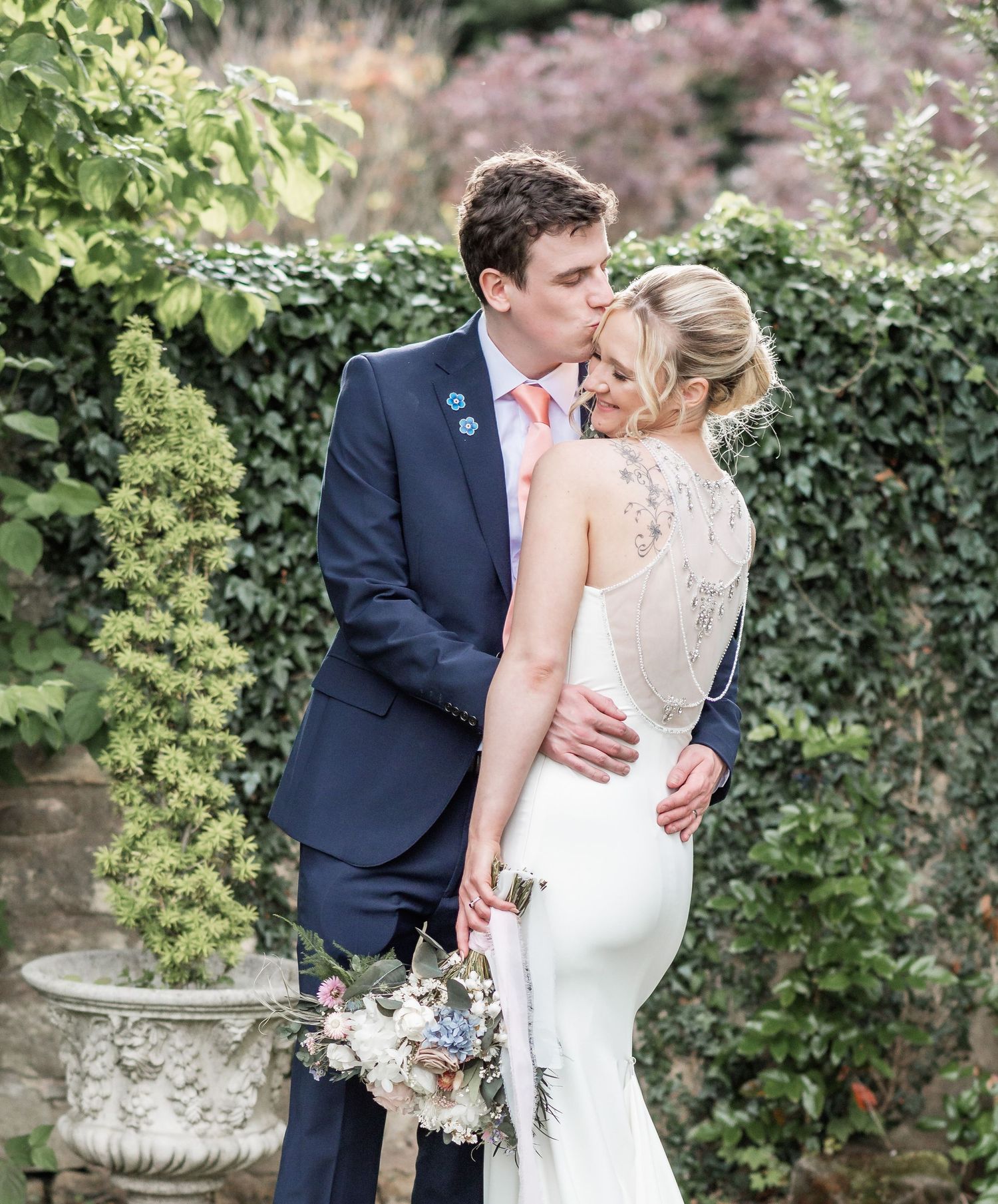 Elegant wedding portrait featuring detailed lace dress against a garden hedge background.
