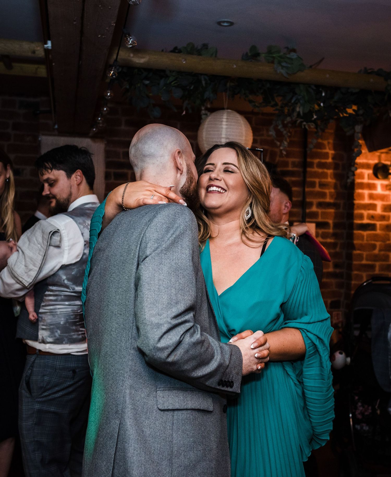 Dancing couple sharing a joyful moment at rustic reception venue with brick walls.