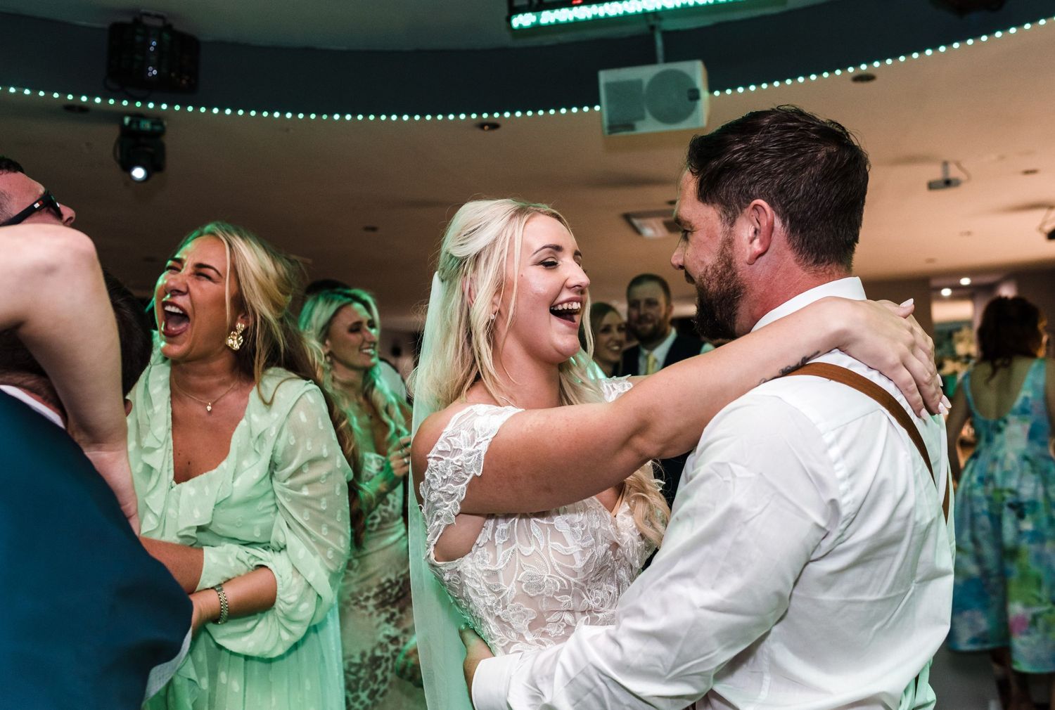 Wedding guests dancing and celebrating on the dance floor with green accent lighting.