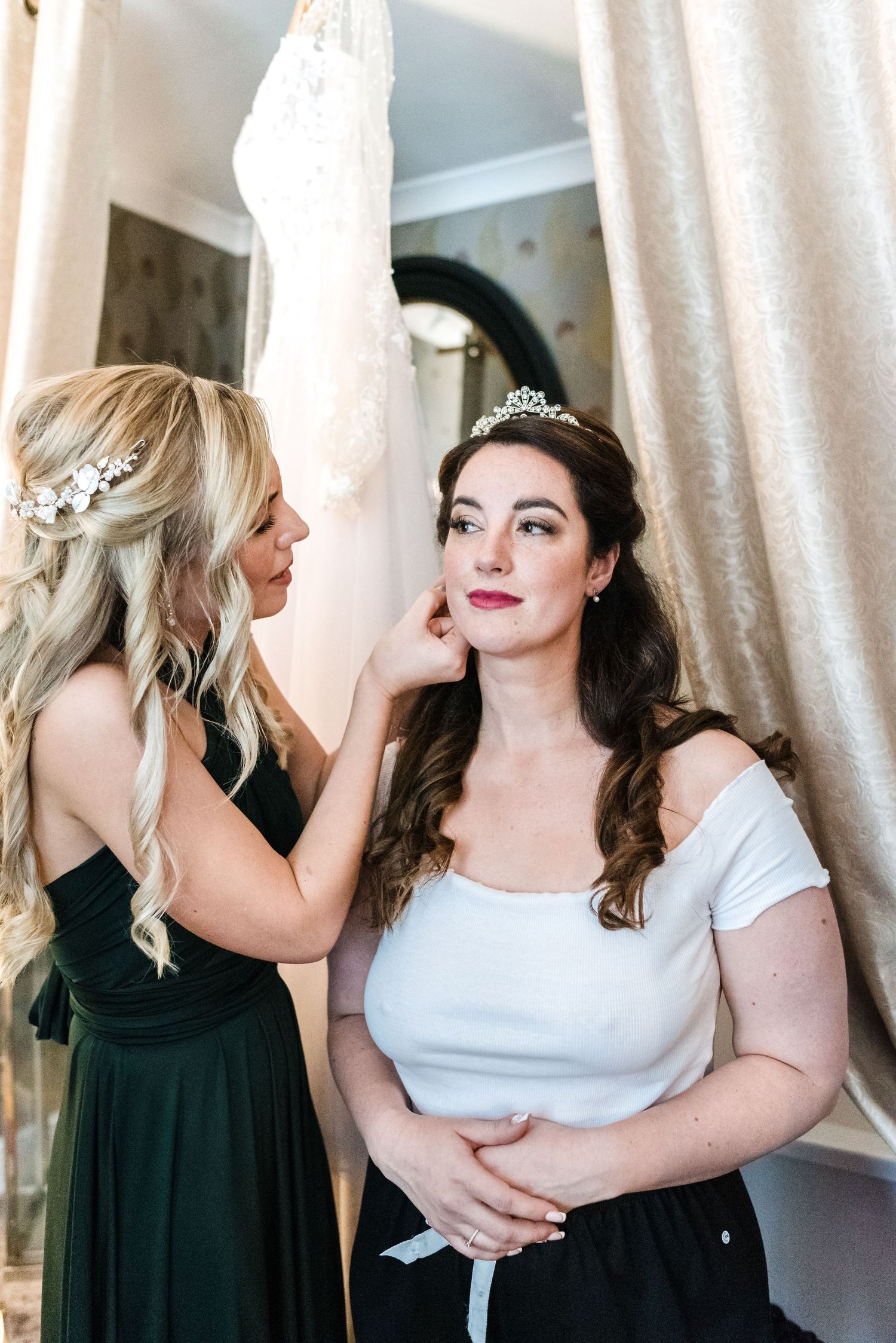 Getting ready scene with makeup application in an elegant room with bridal gown hanging in background.