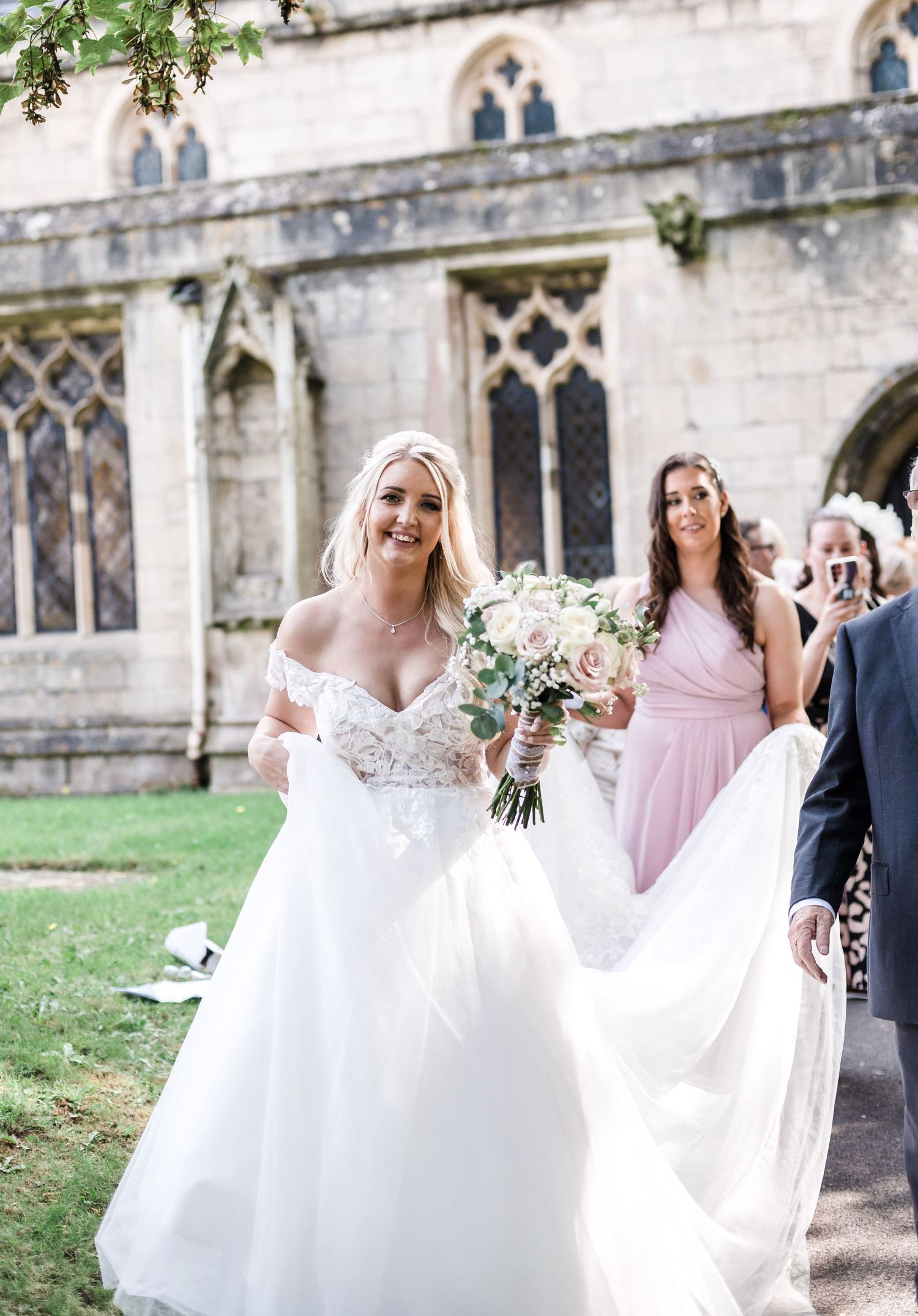 Elegant bride in white gown walking outside historic church building.