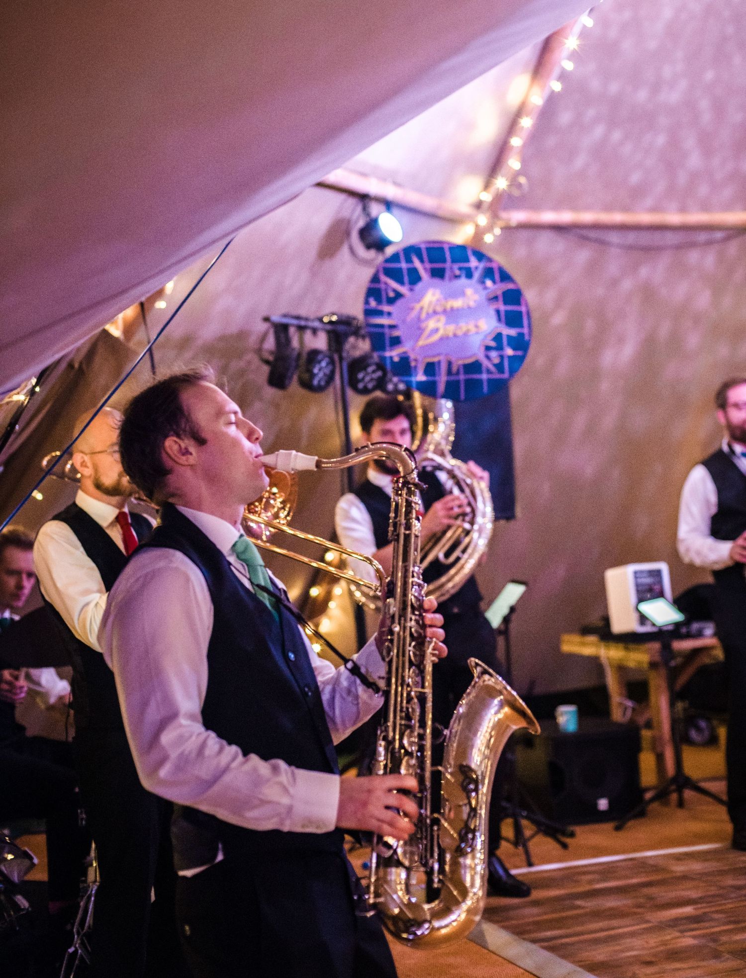 Musicians performing at a wedding reception with a saxophone player in focus under string lights.