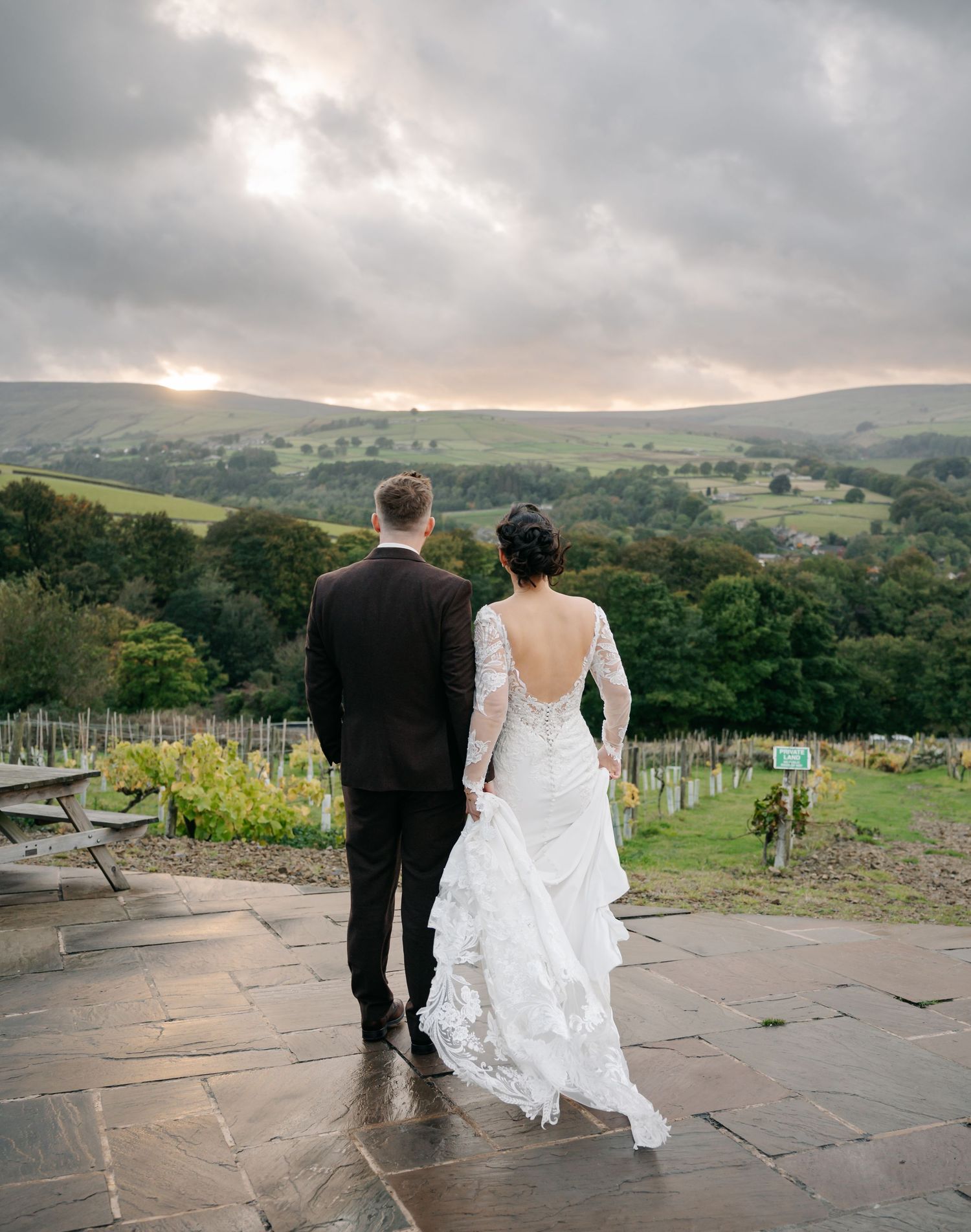 Couple overlooks scenic countryside view at sunset from stone patio in wedding attire.