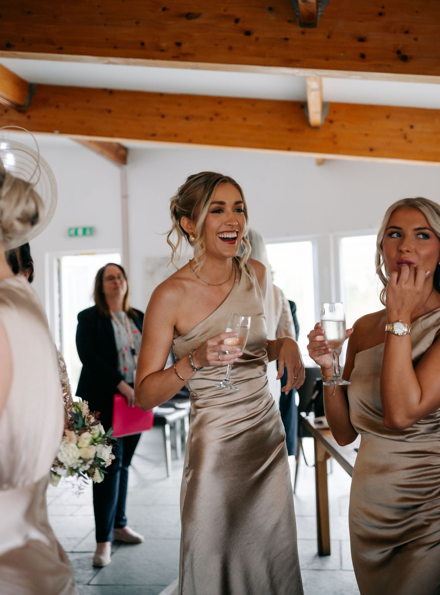 Wedding party members in champagne colored dresses share laughs and candid moments at a reception.