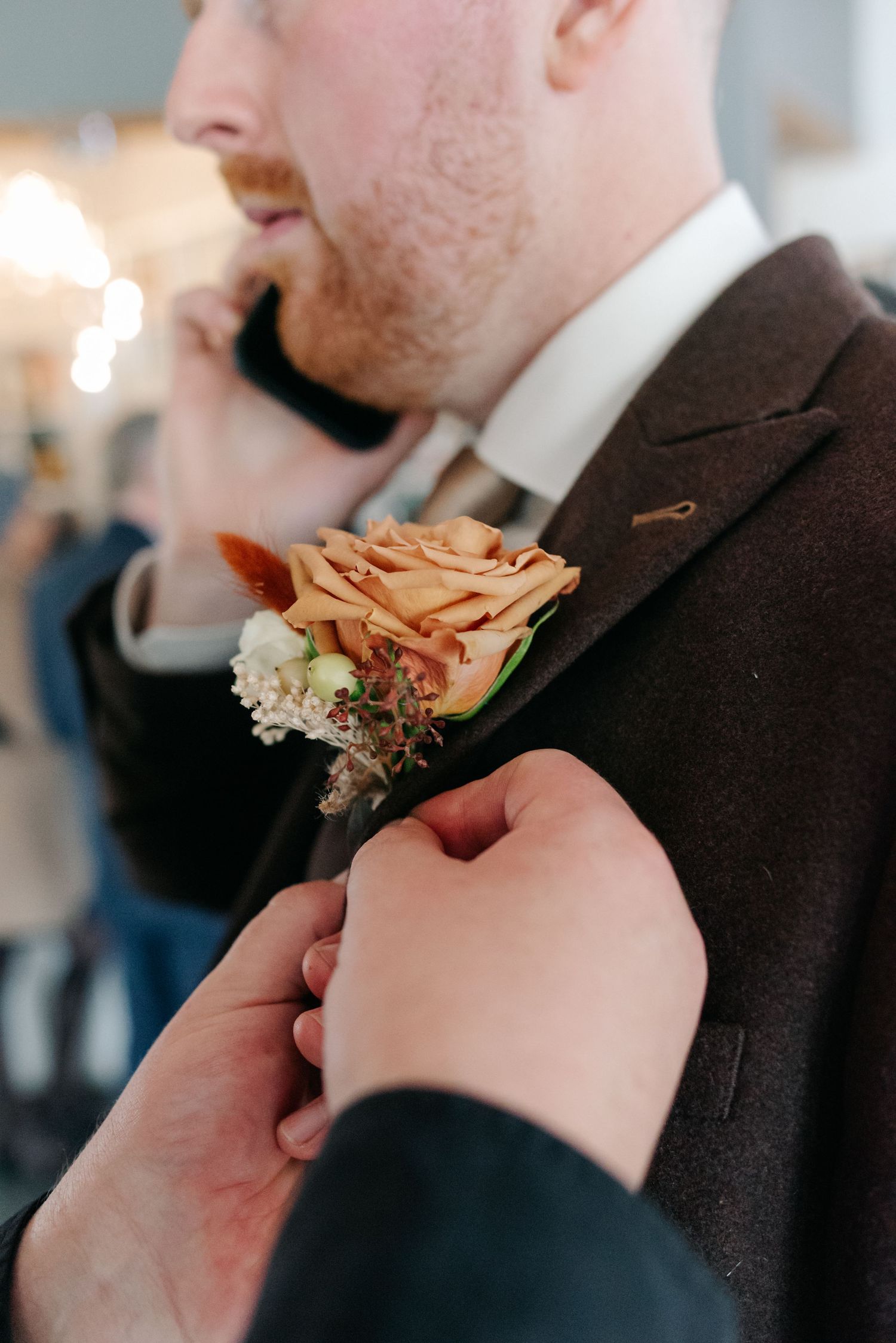 Close-up of a peach-colored boutonniere being pinned to a dark suit jacket.