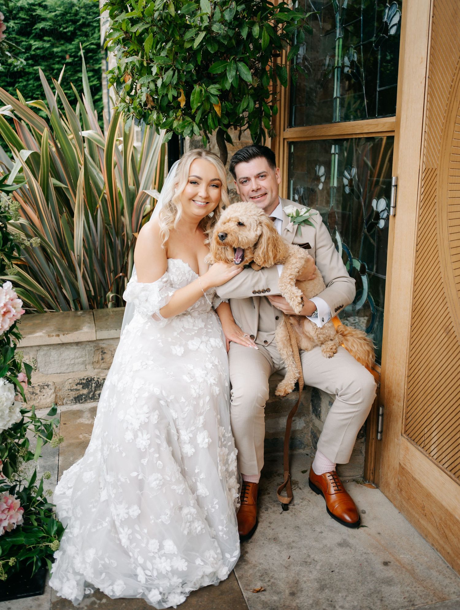 Wedding couple posing with their dogs outside a venue with greenery.