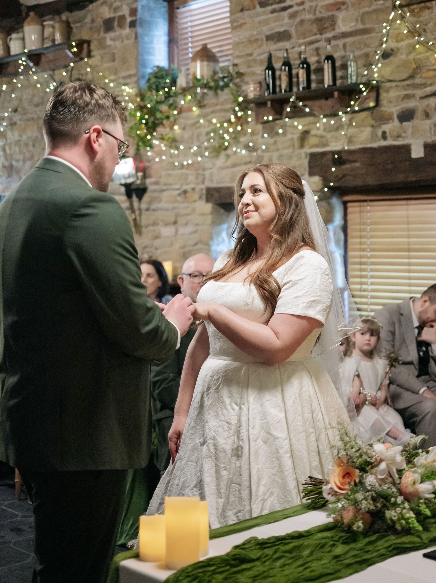 Wedding ceremony in a rustic stone venue with twinkling lights and greenery decorations.