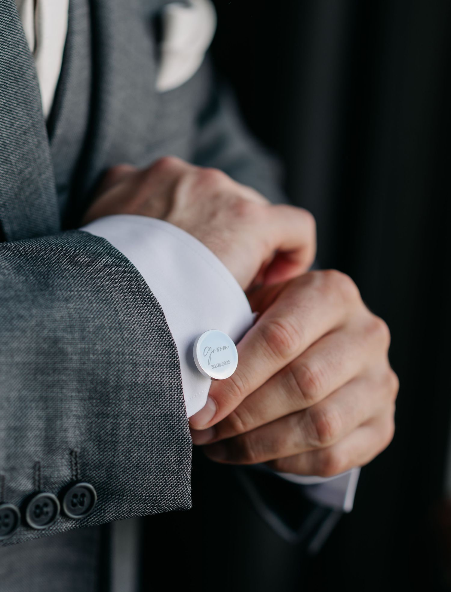 Close-up shot of hands adjusting cufflinks on a gray suit sleeve.