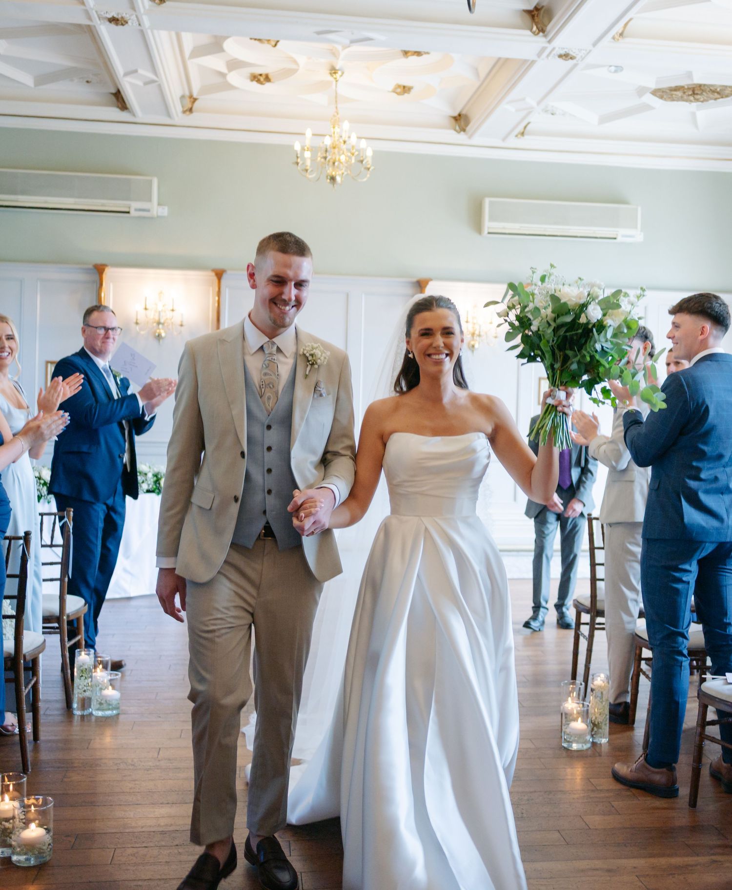 Wedding guests in formal attire mingling and celebrating in an elegant reception venue with chandeliers.