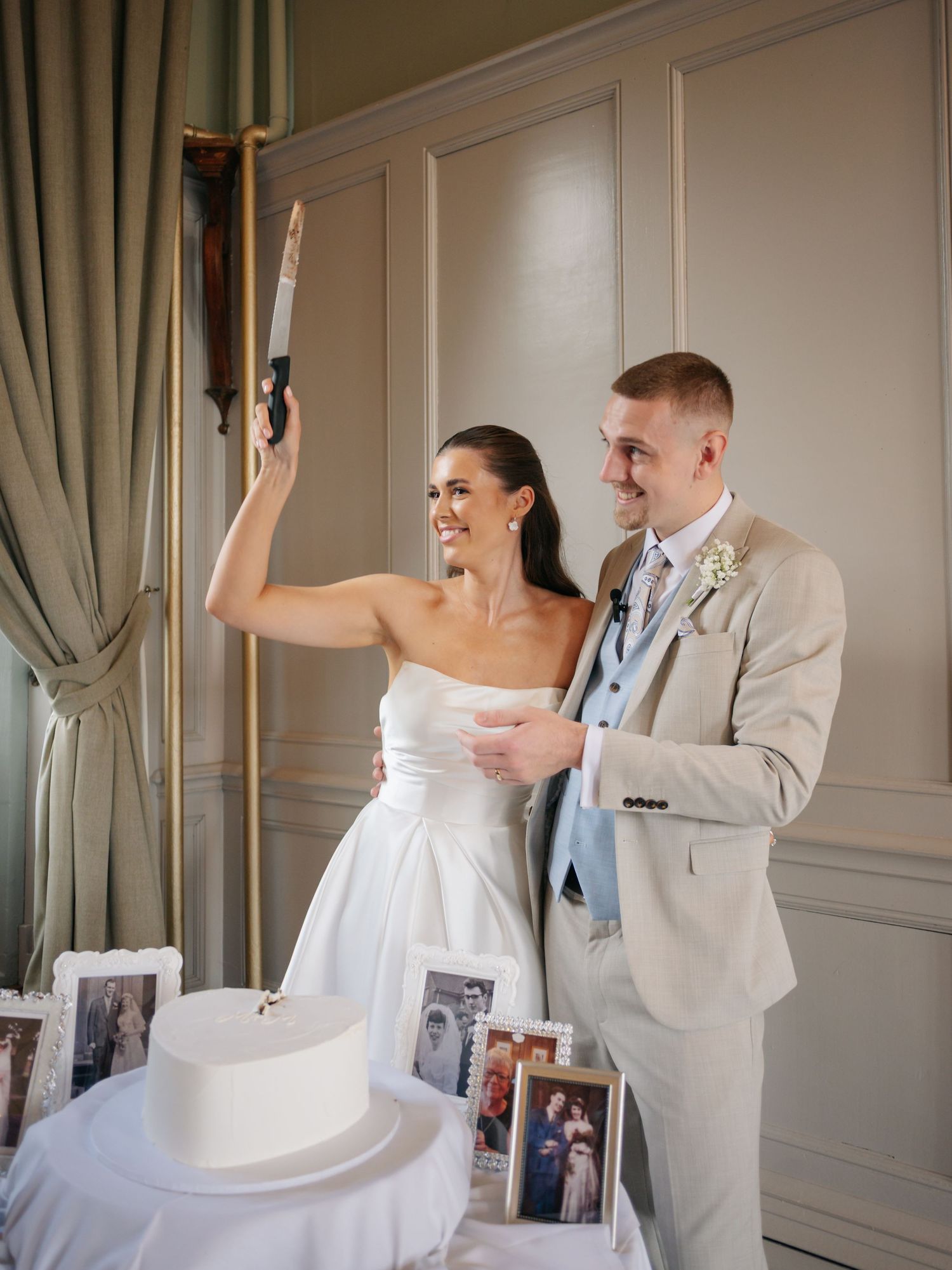 Couple laughs together during wedding celebrations in a formal room with curtains.