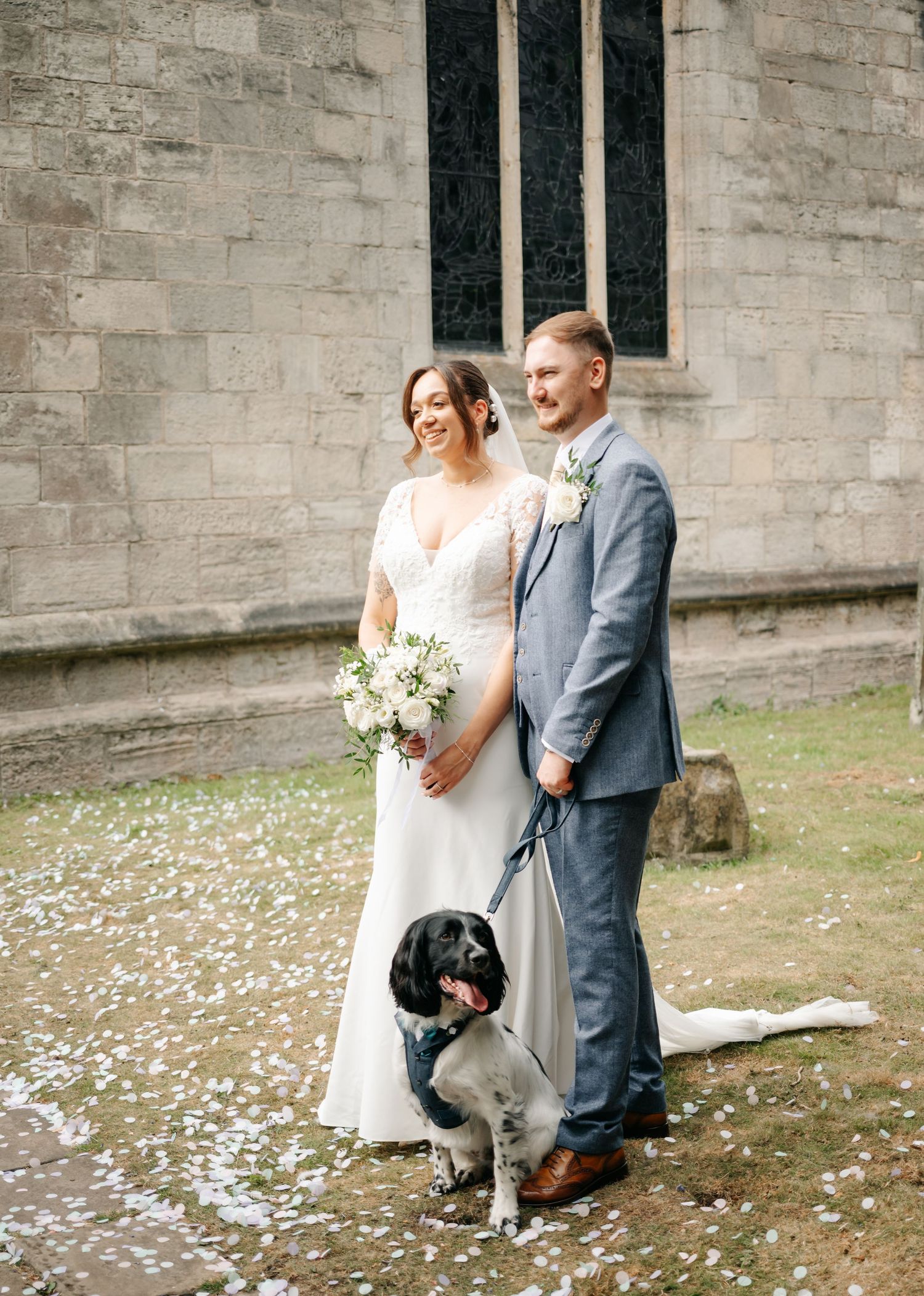 Couple walking together on confetti-covered ground outside a stone building after their wedding ceremony.