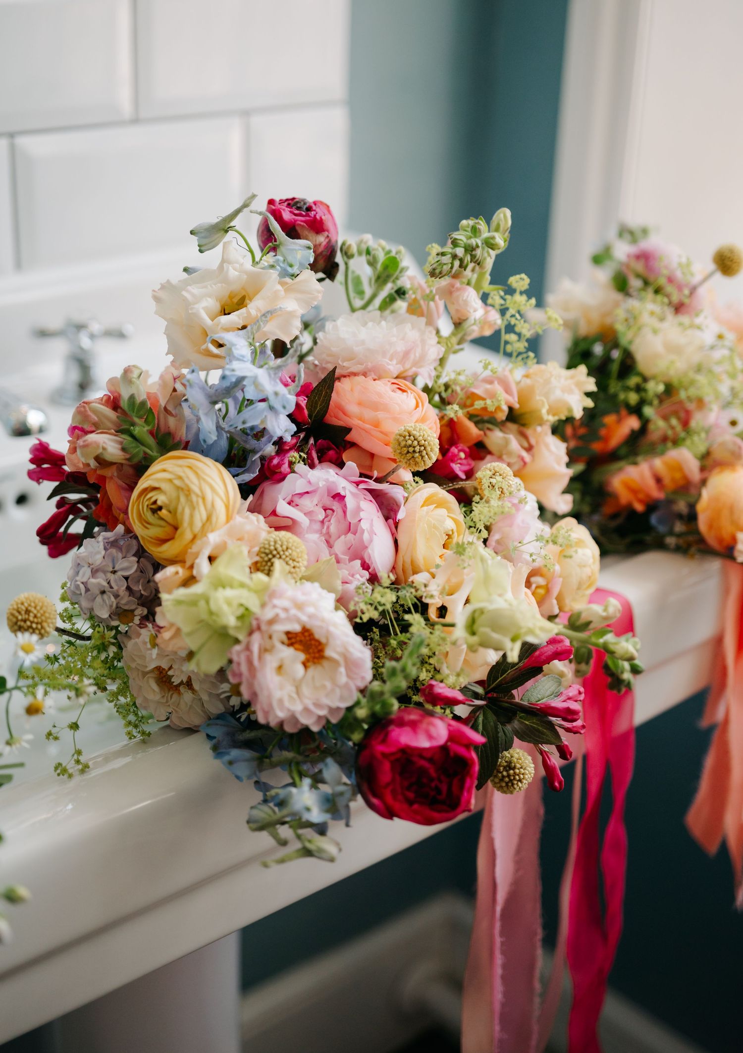 Colorful wedding bouquets with pink, orange, and white flowers lined up on a white shelf with flowing ribbons.