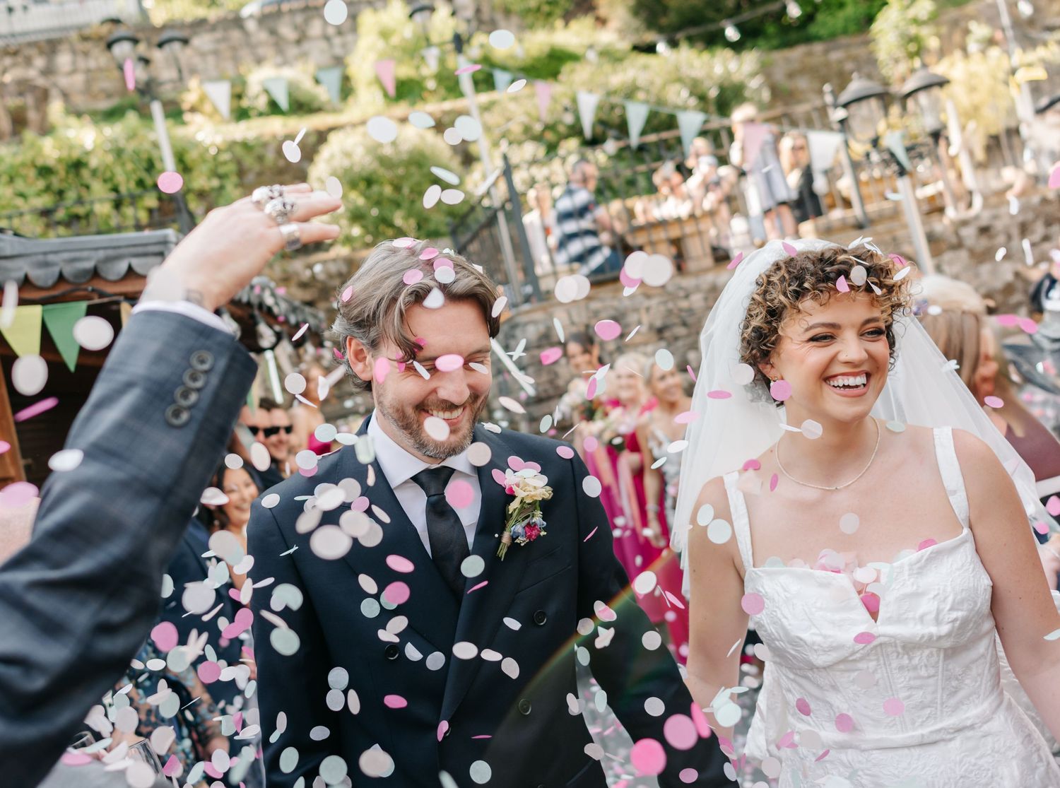 A joyful wedding celebration with confetti being thrown in a garden setting.