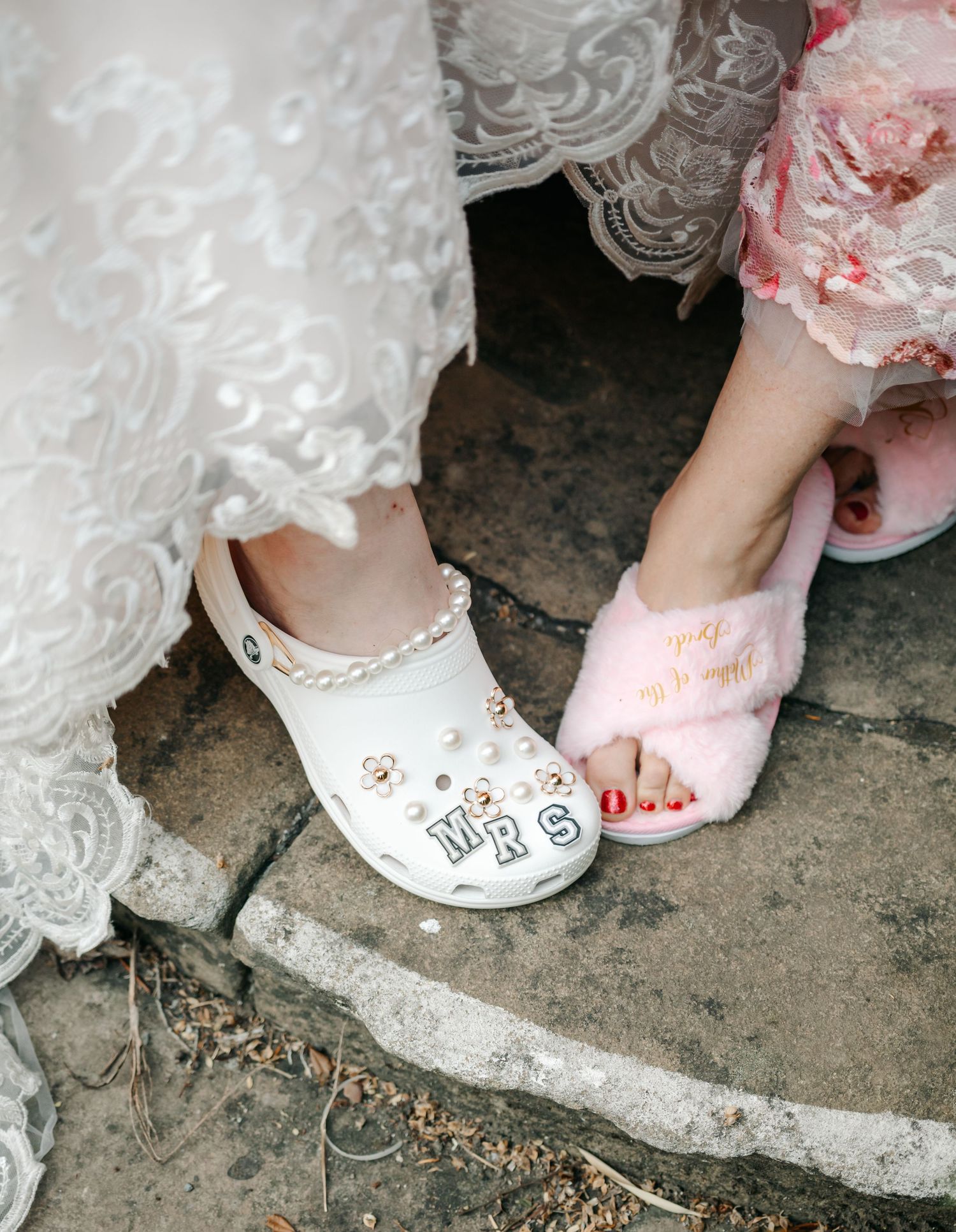 Bride wearing decorated white Crocs with MRS charms beside bridesmaid in pink fluffy slippers.