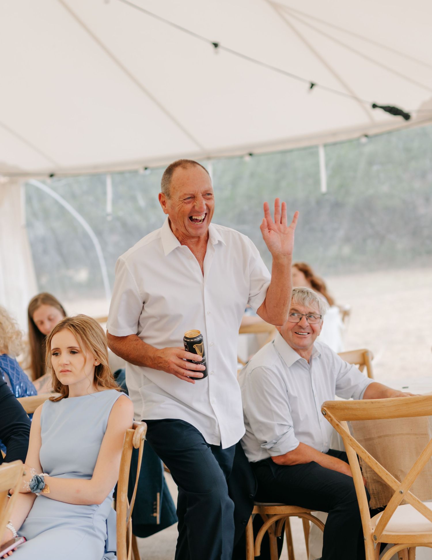 Wedding guests enjoying themselves under a white tent at an outdoor reception celebration.