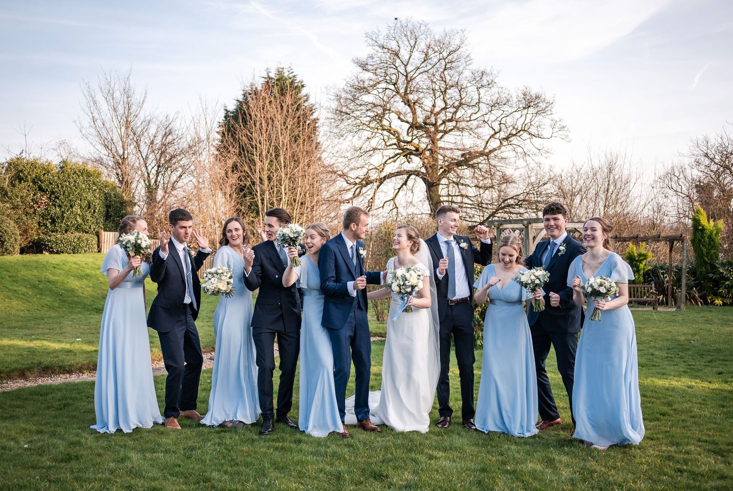 Wedding party in navy suits and light blue dresses posed together outdoors.