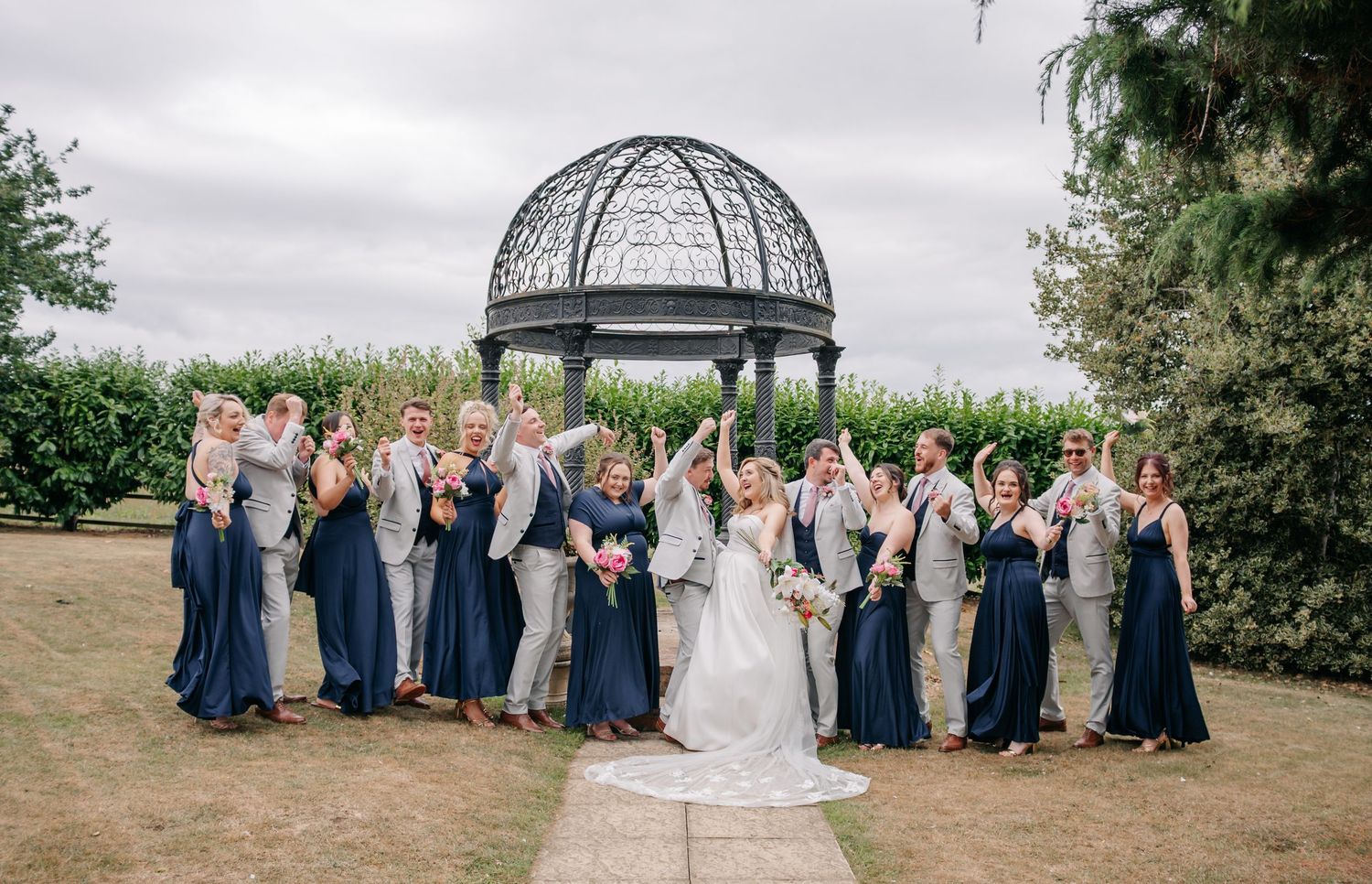 Large wedding party gathered for formal photos in a garden setting with navy blue attire.