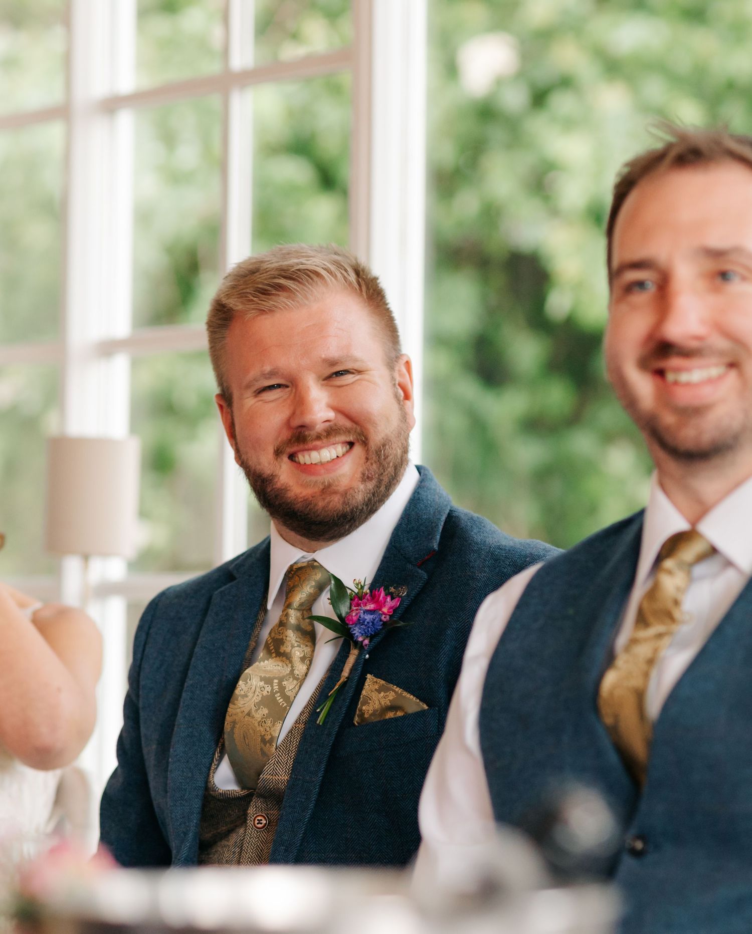 Groomsmen in navy suits with gold ties share a laugh during wedding reception.