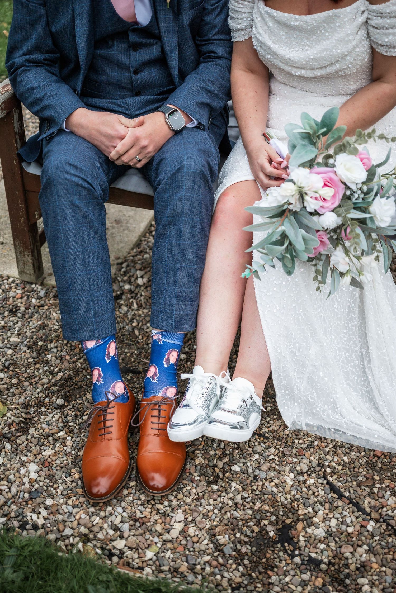 Wedding couple's feet showing fun socks and shoes while sitting on garden bench with bridal bouquet.