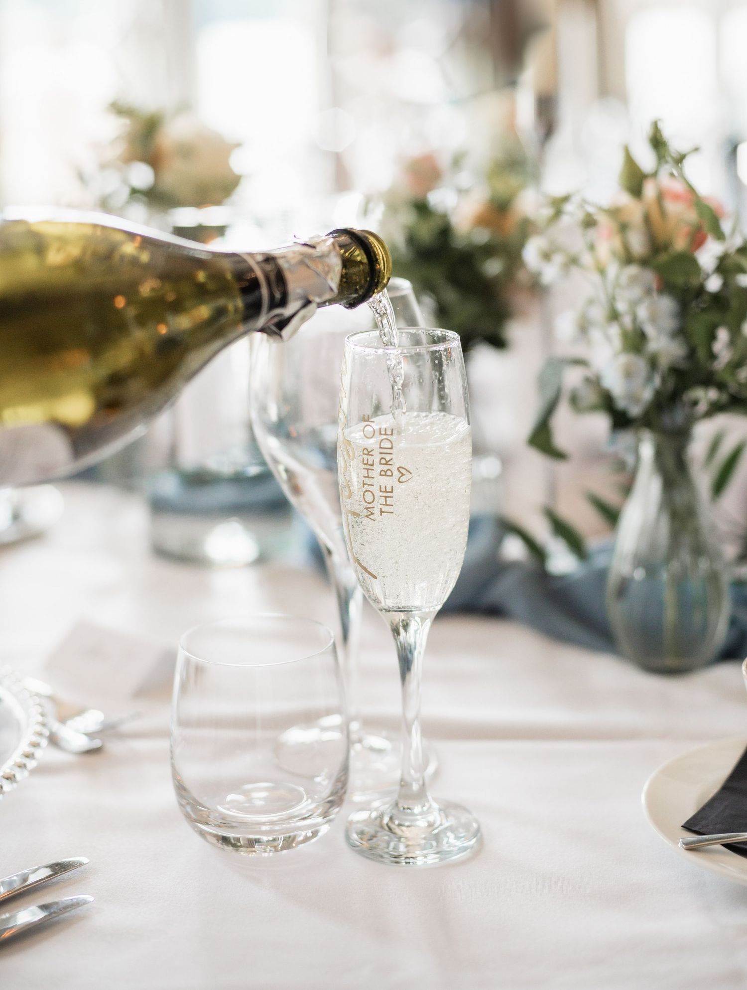 Champagne being poured into delicate flutes on an elegant wedding table decorated with floral arrangements.