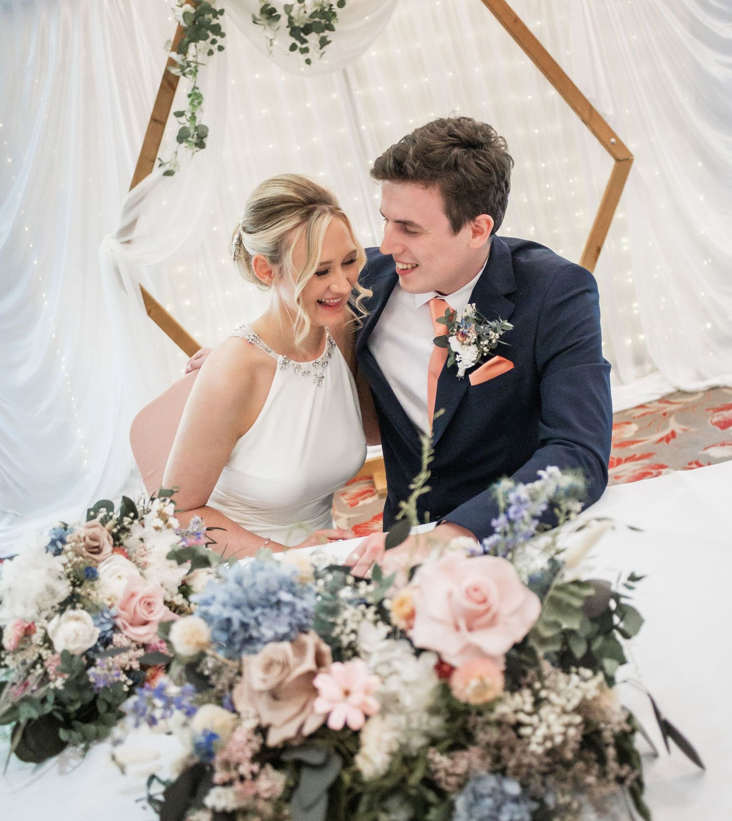 Romantic moment between newlyweds with floral arch and pink and blue flower arrangements.