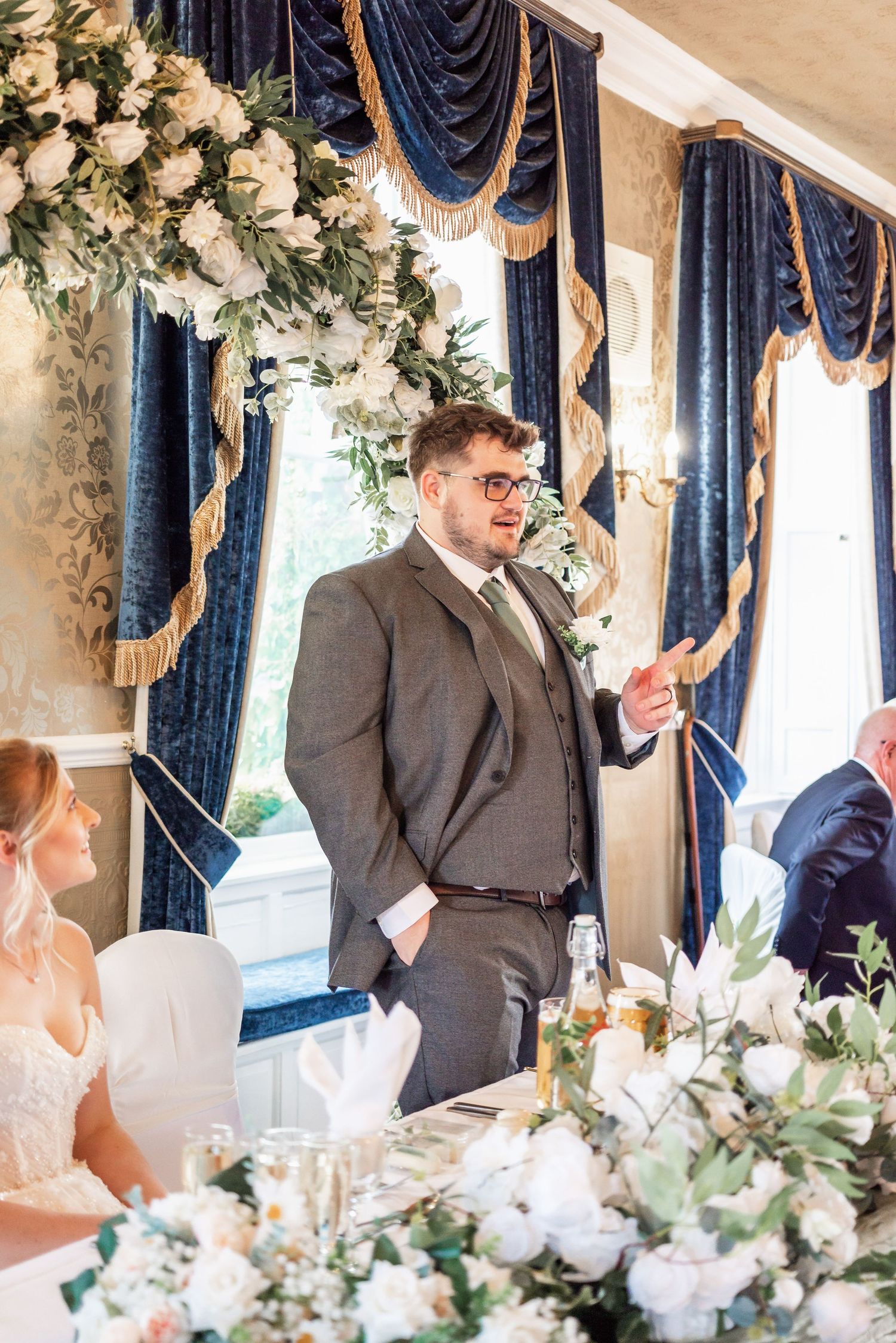 Wedding reception in elegant room with navy blue drapes and floral decorations.