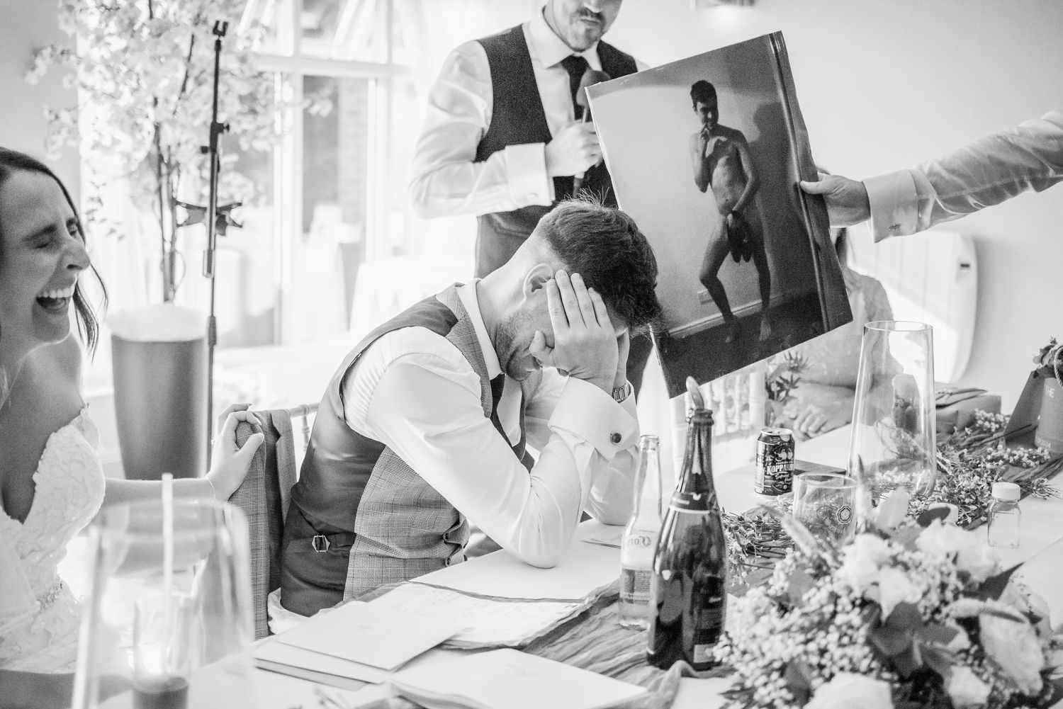 Black and white photo of emotional wedding speeches with guests looking at photographs during reception dinner.