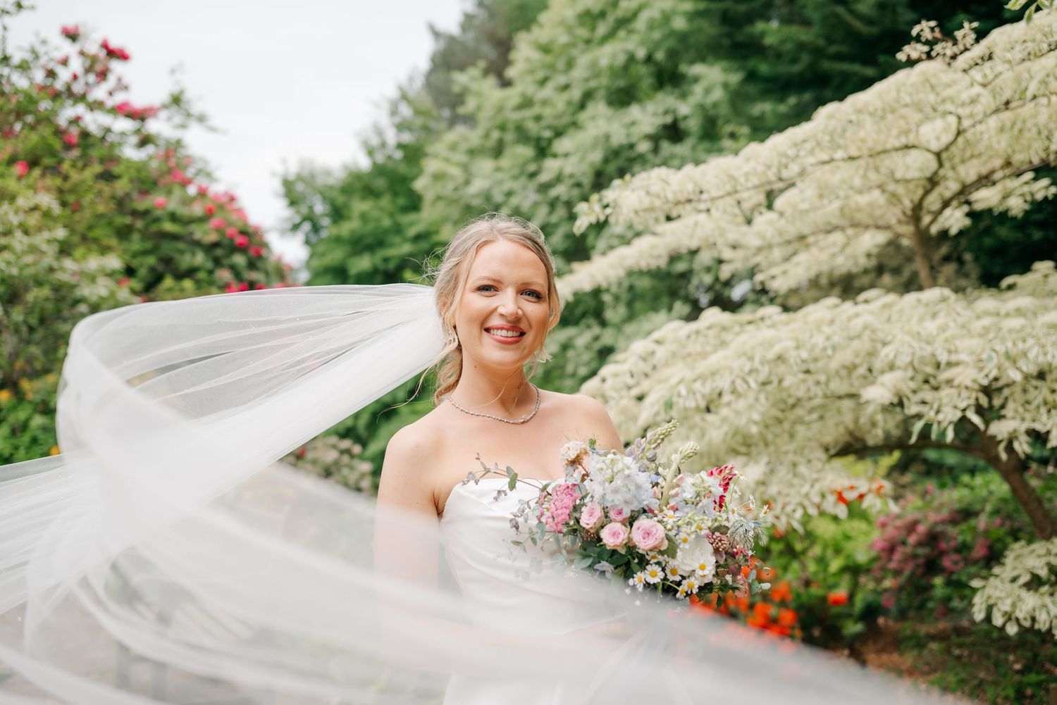 Flowing veil catches the breeze in a garden setting with blooming flowers.