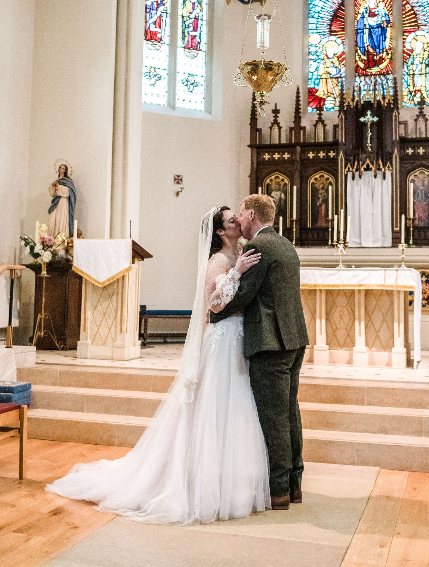 Newlyweds share their first kiss at the altar with stained glass windows in background.