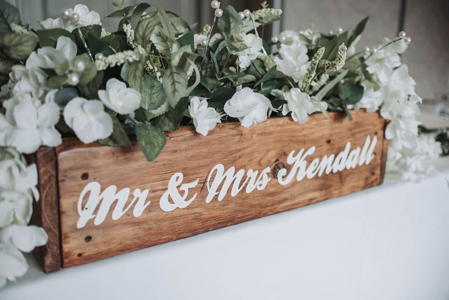 Rustic wooden wedding sign with white floral decorations displaying Mr & Mrs Kendall.