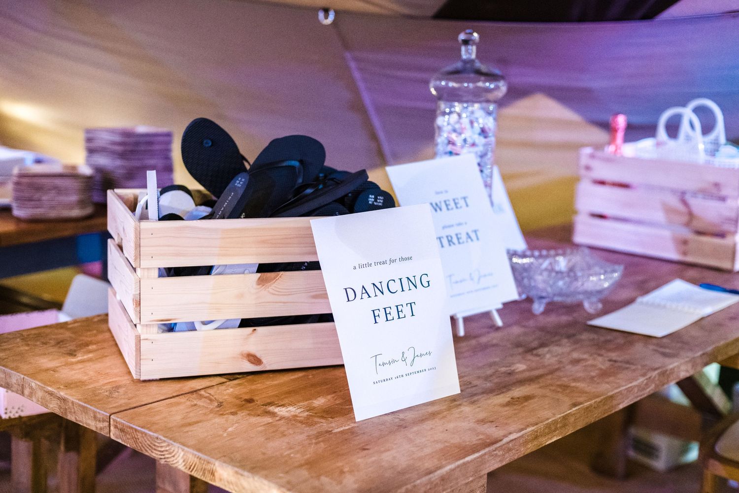 A wooden crate labeled 'Dancing Feet' with flip flops displayed at a wedding reception.