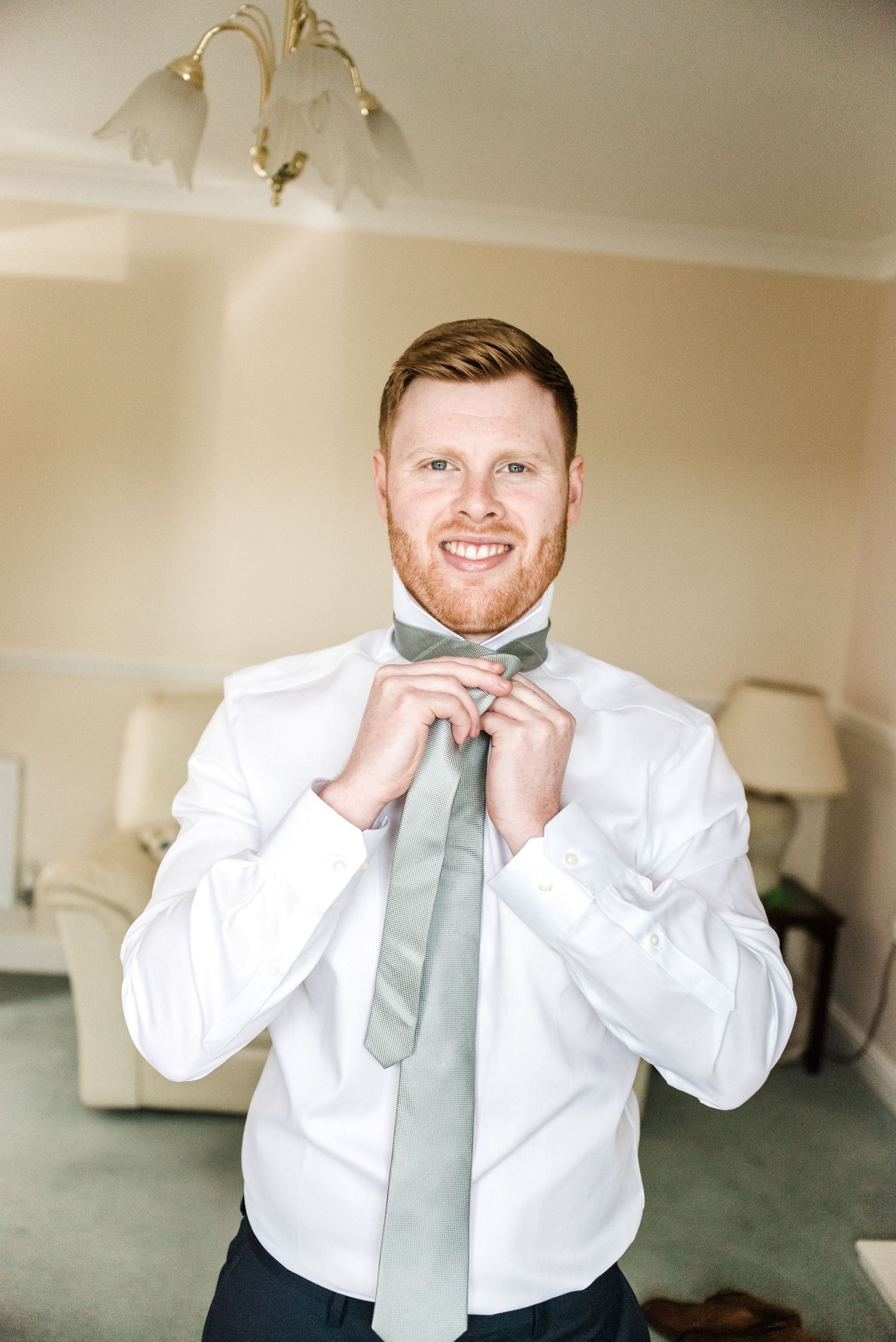 A person adjusts a mint green tie while wearing a crisp white dress shirt.