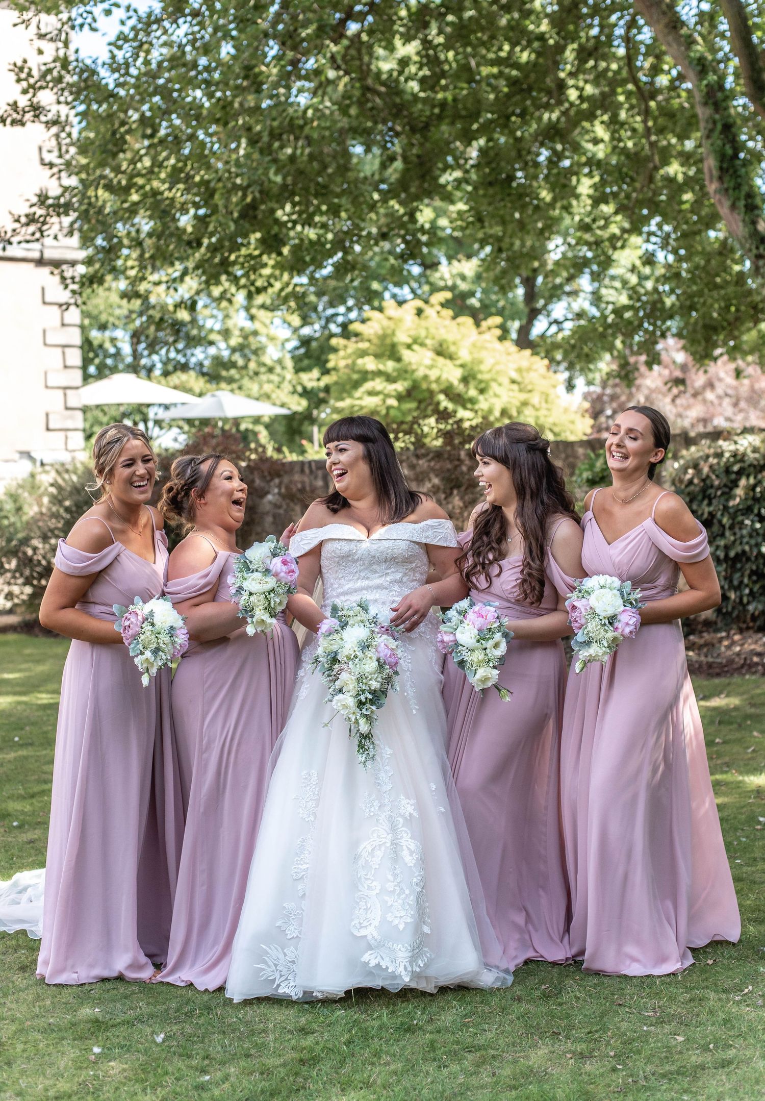 Bridesmaids in flowing dusty pink dresses share a laugh during wedding photos.