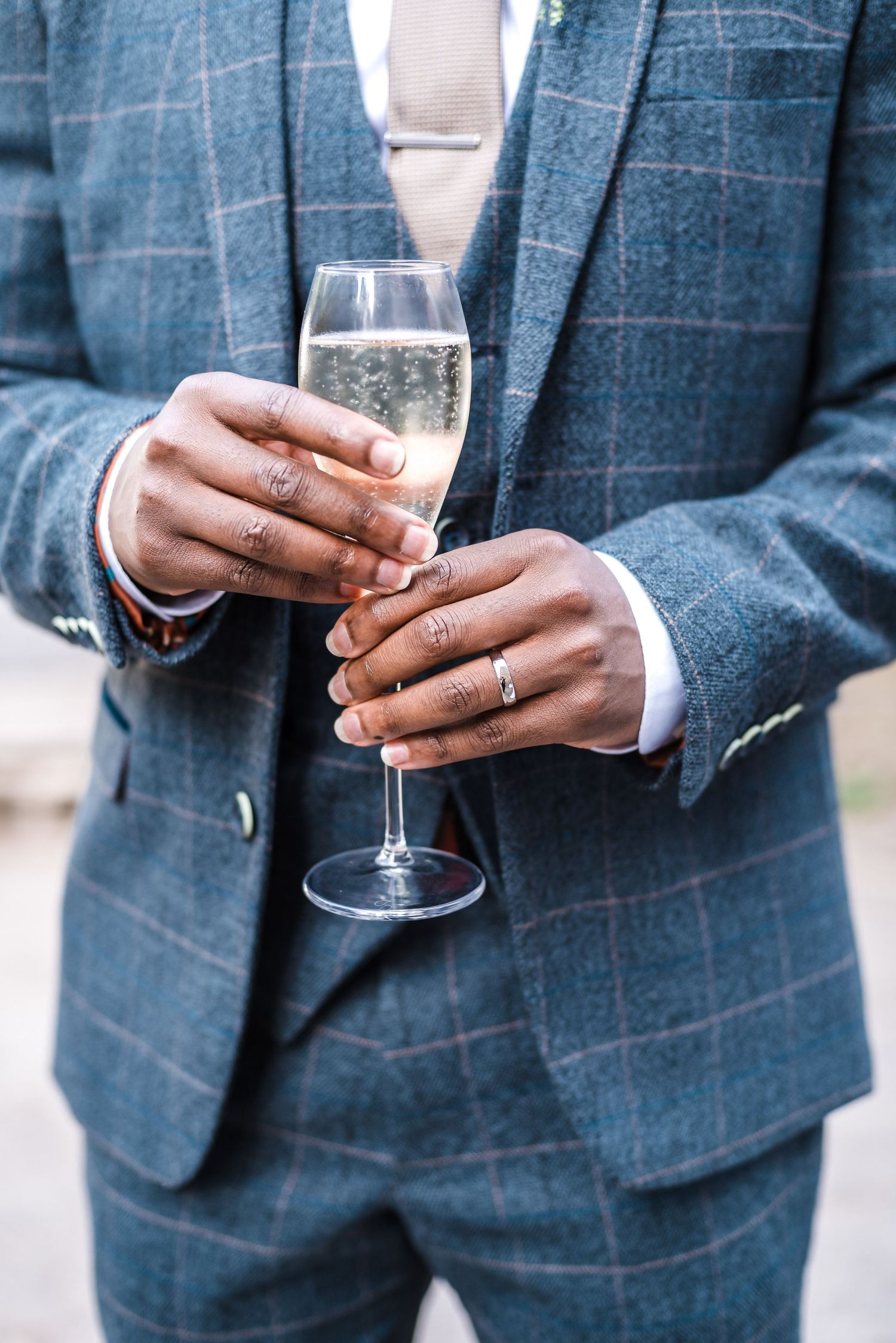 Close up of hands holding a champagne flute while wearing a navy windowpane suit.