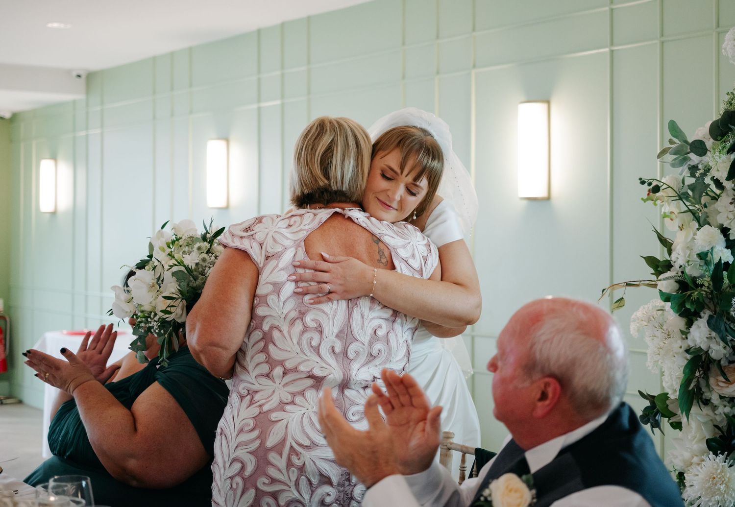 Joyful wedding celebration with guests dancing and embracing in a bright indoor venue.