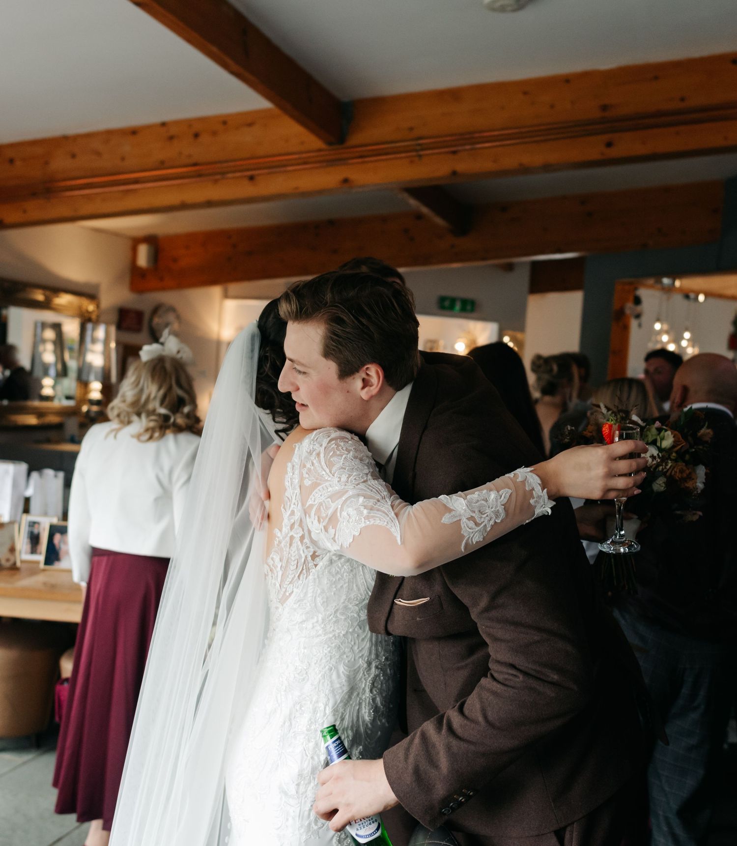 Wedding celebration moment with guests embracing while holding drinks in a rustic venue.