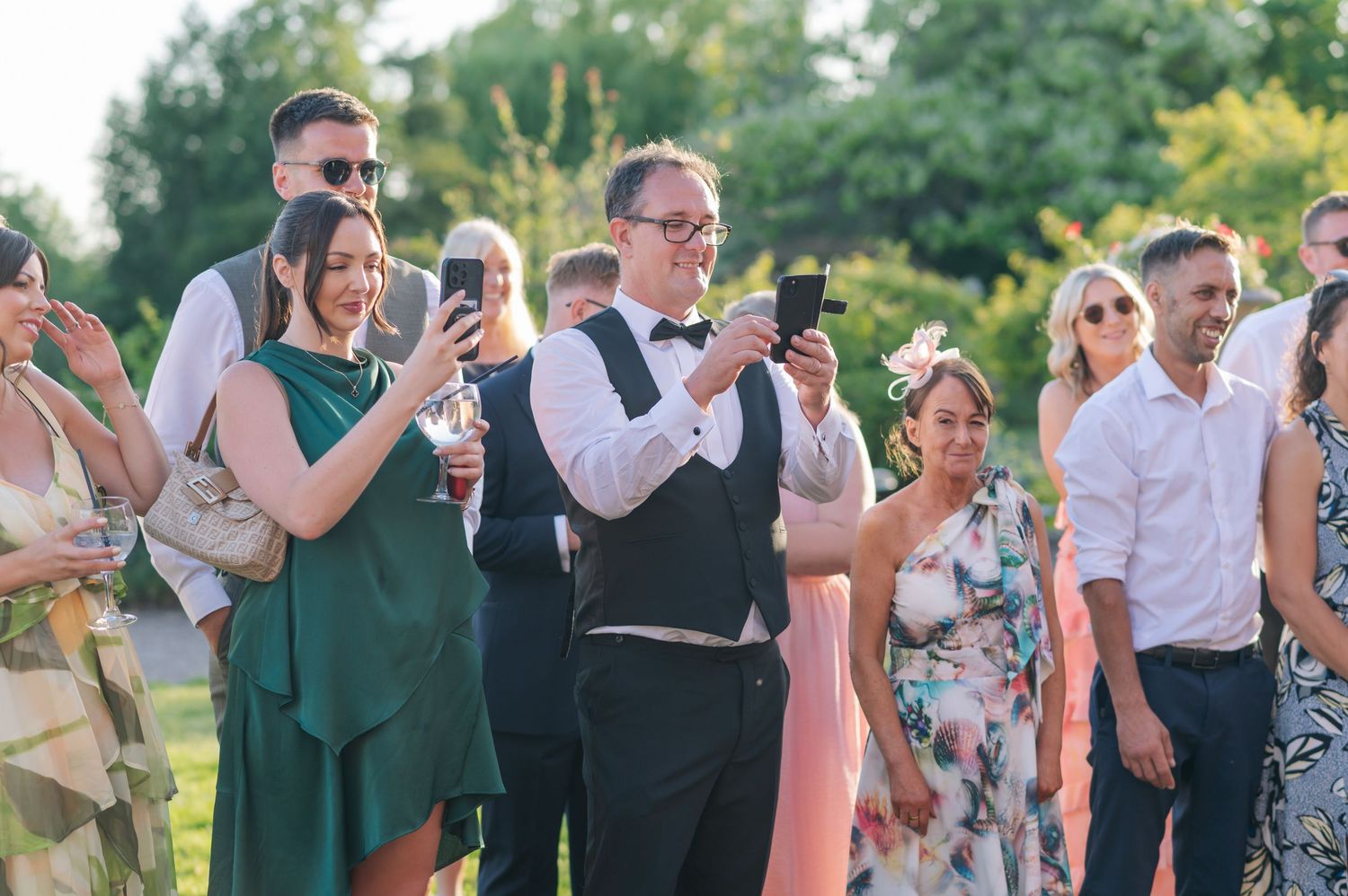 Wedding guests in formal attire mingle and socialize during an outdoor garden reception.