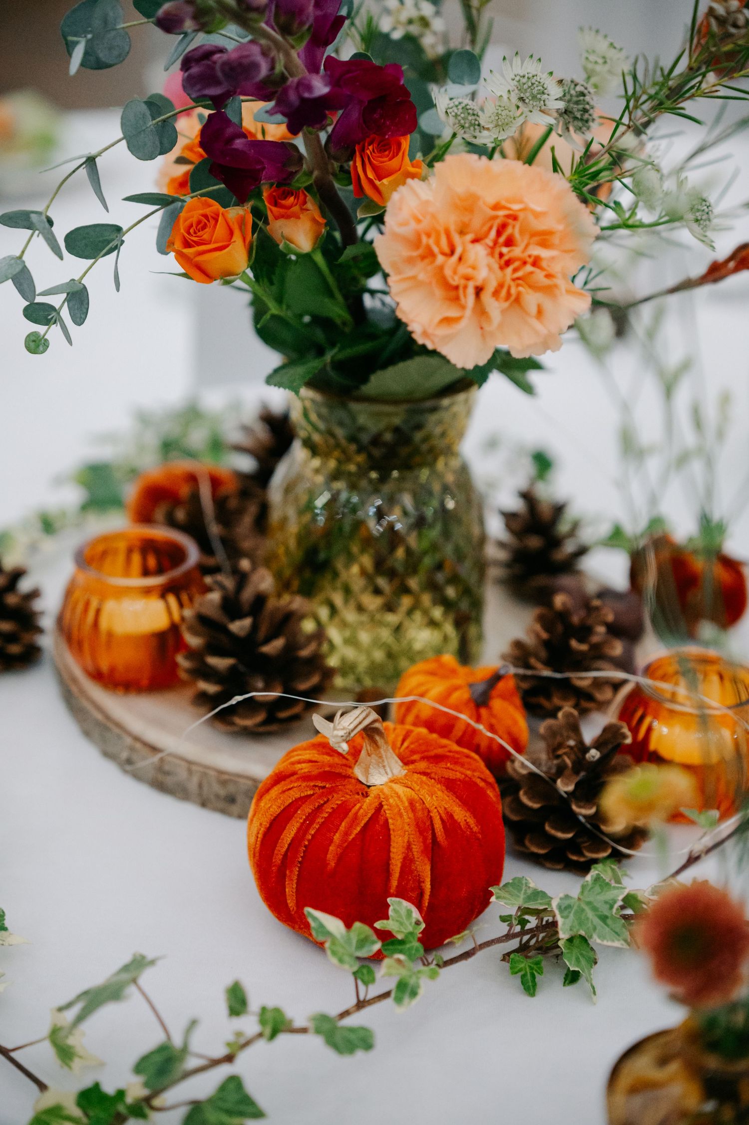 Autumn wedding table decor with orange pumpkins, pinecones, and colorful floral arrangements.