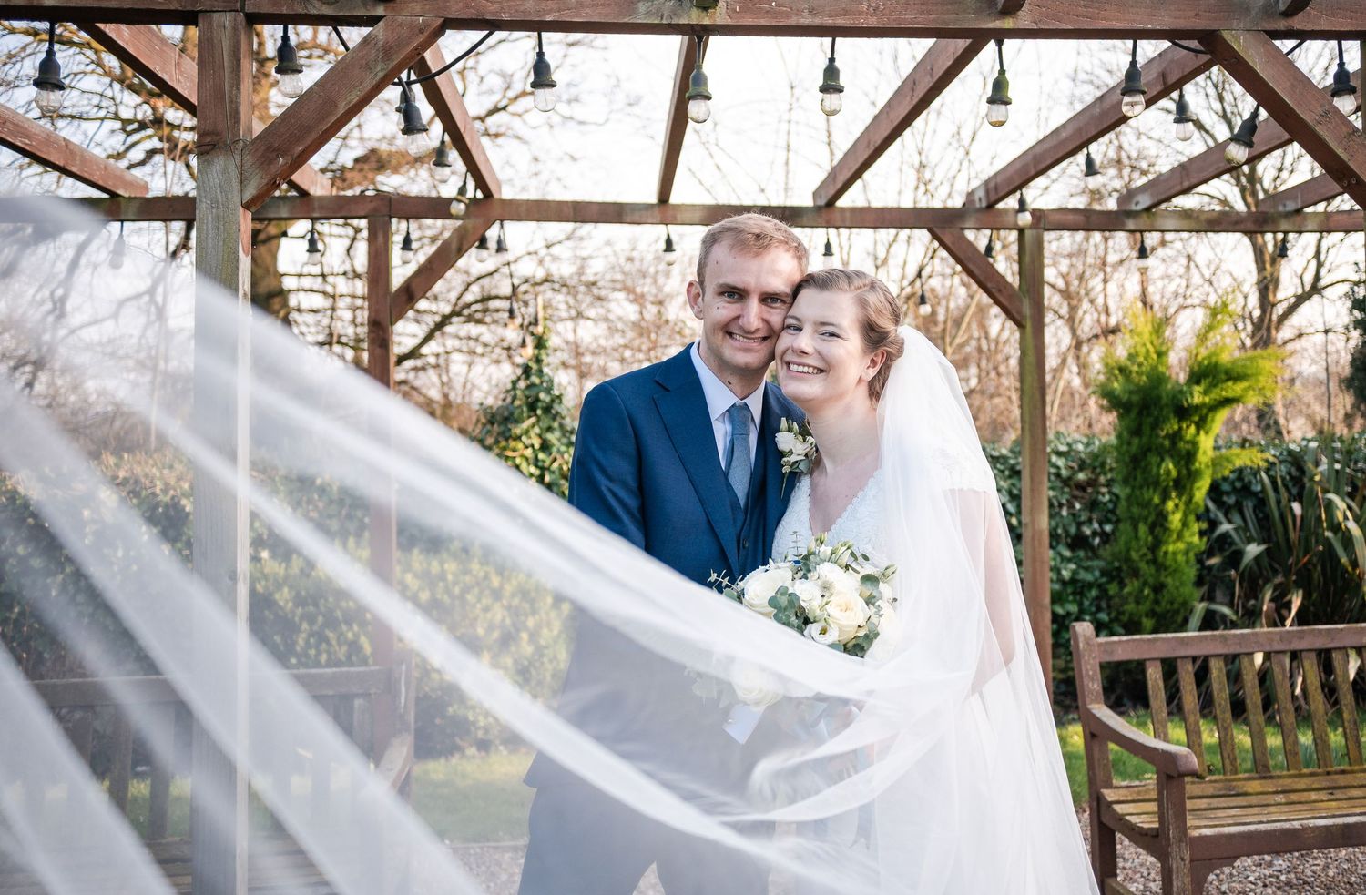 Rustic wooden pergola decorated for a wedding ceremony with hanging lights and floral arrangements.