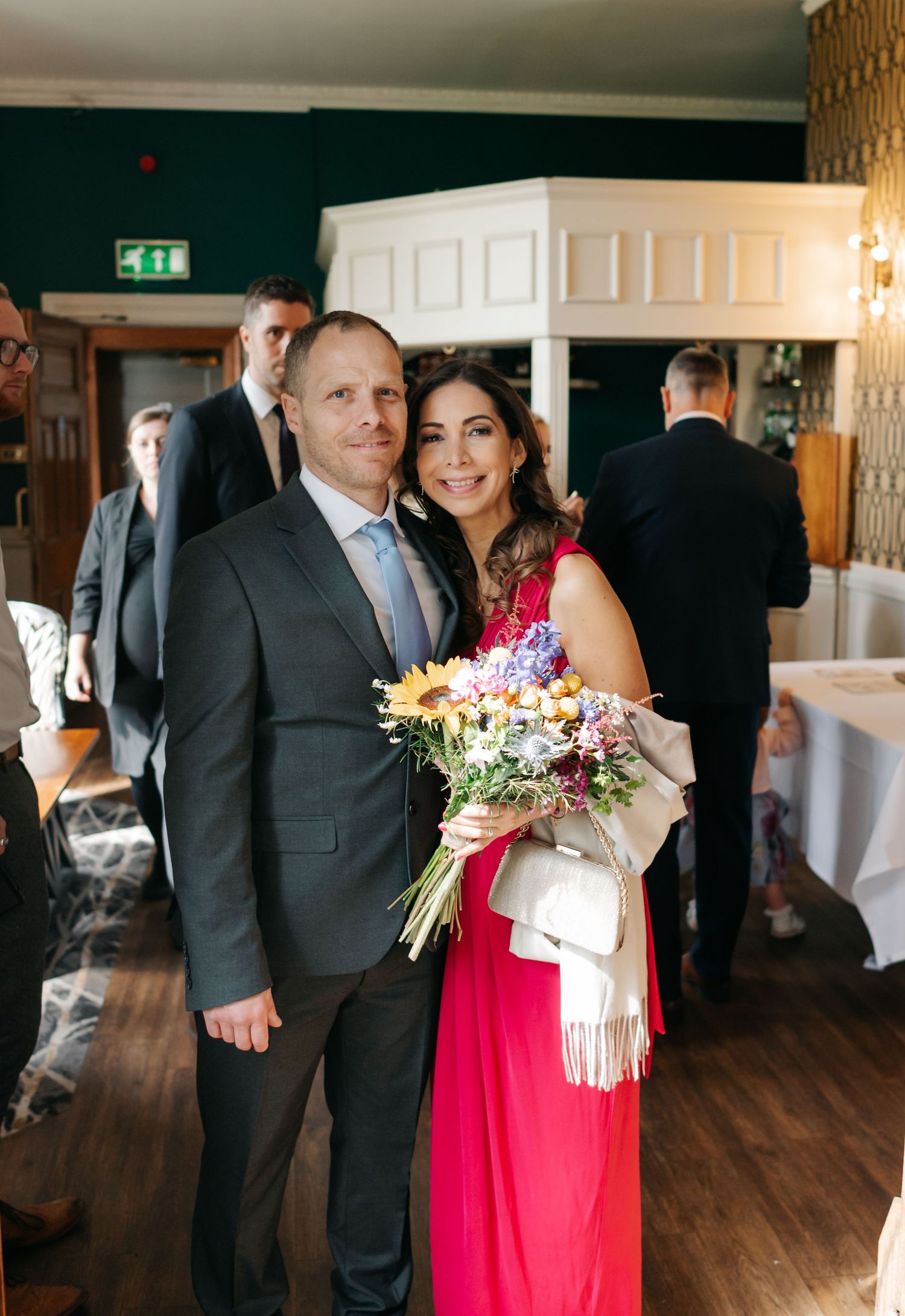 Wedding party members in formal attire gathering in an elegant wood-paneled reception room with white decor.