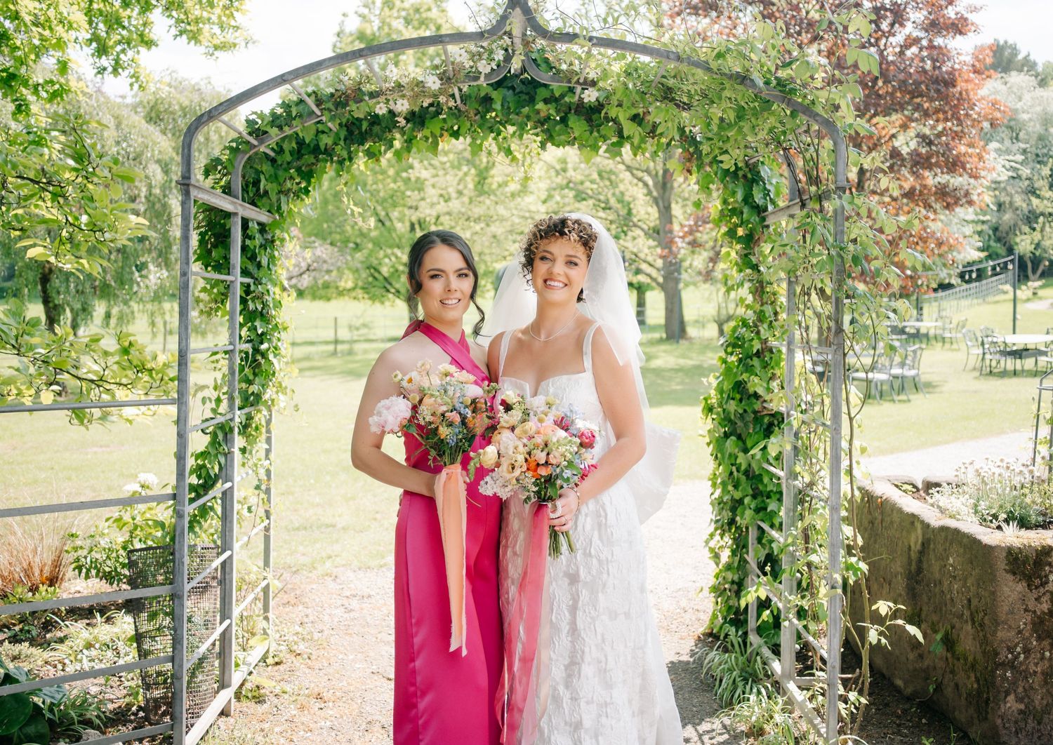 Two people pose under a flower-covered garden arch during a wedding celebration.