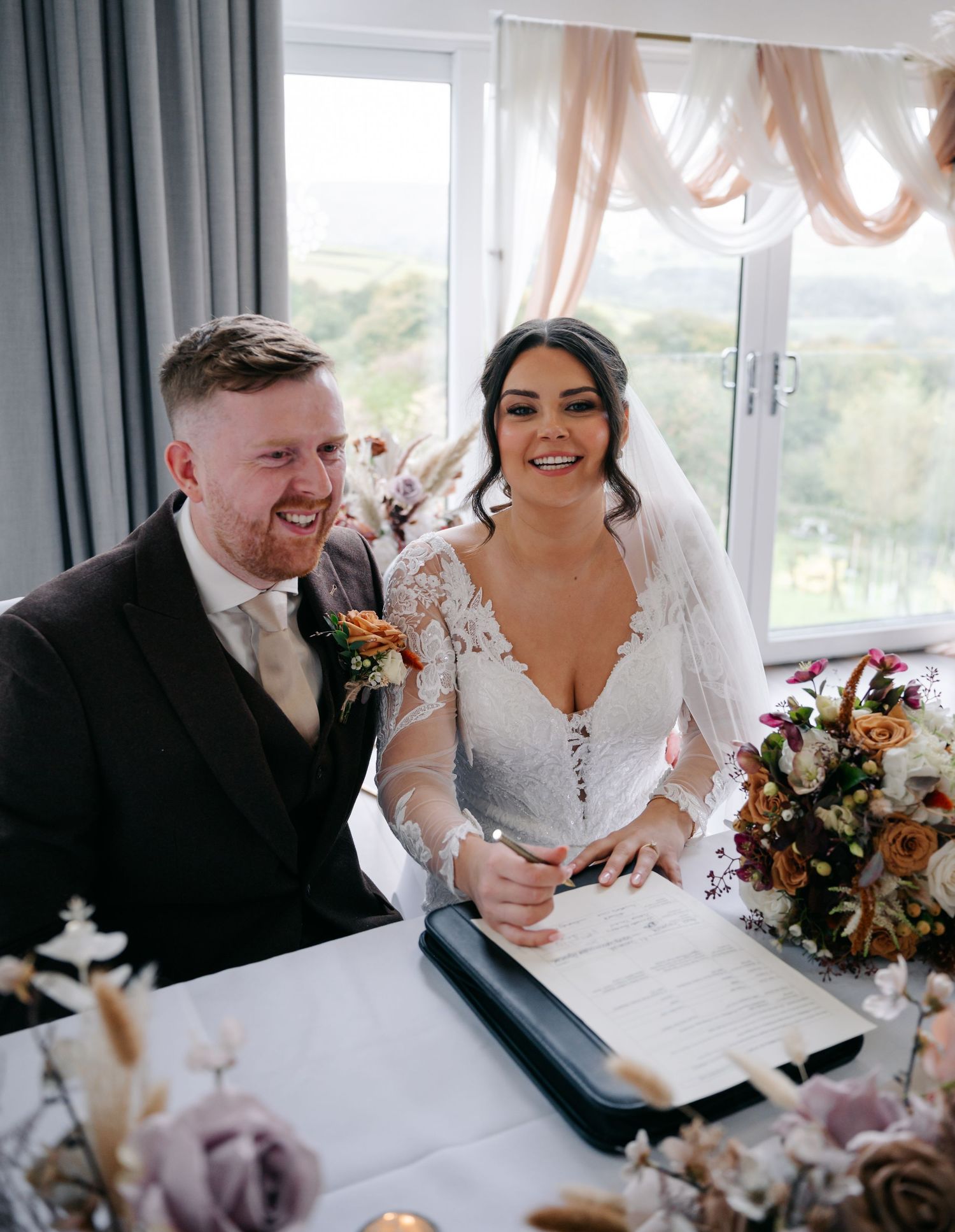 Wedding reception scene with white decor and floral arrangements in a bright, window-lit venue.