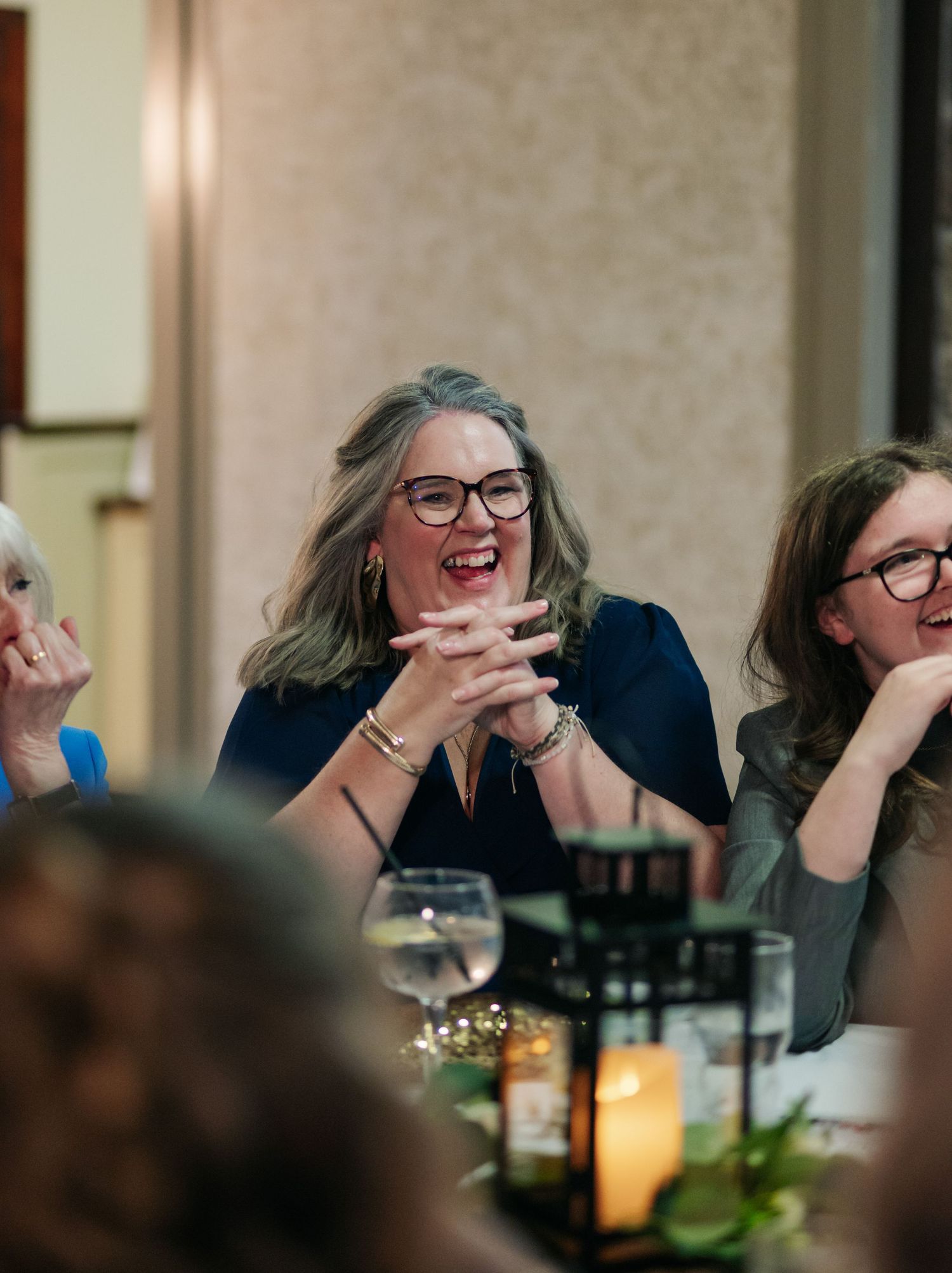 Joyful candid moments captured during an evening dinner reception with warm lighting.