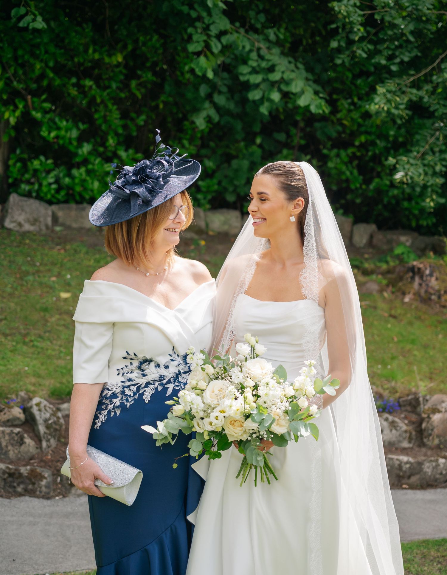 Wedding party members in navy and white dresses holding floral bouquets outdoors.