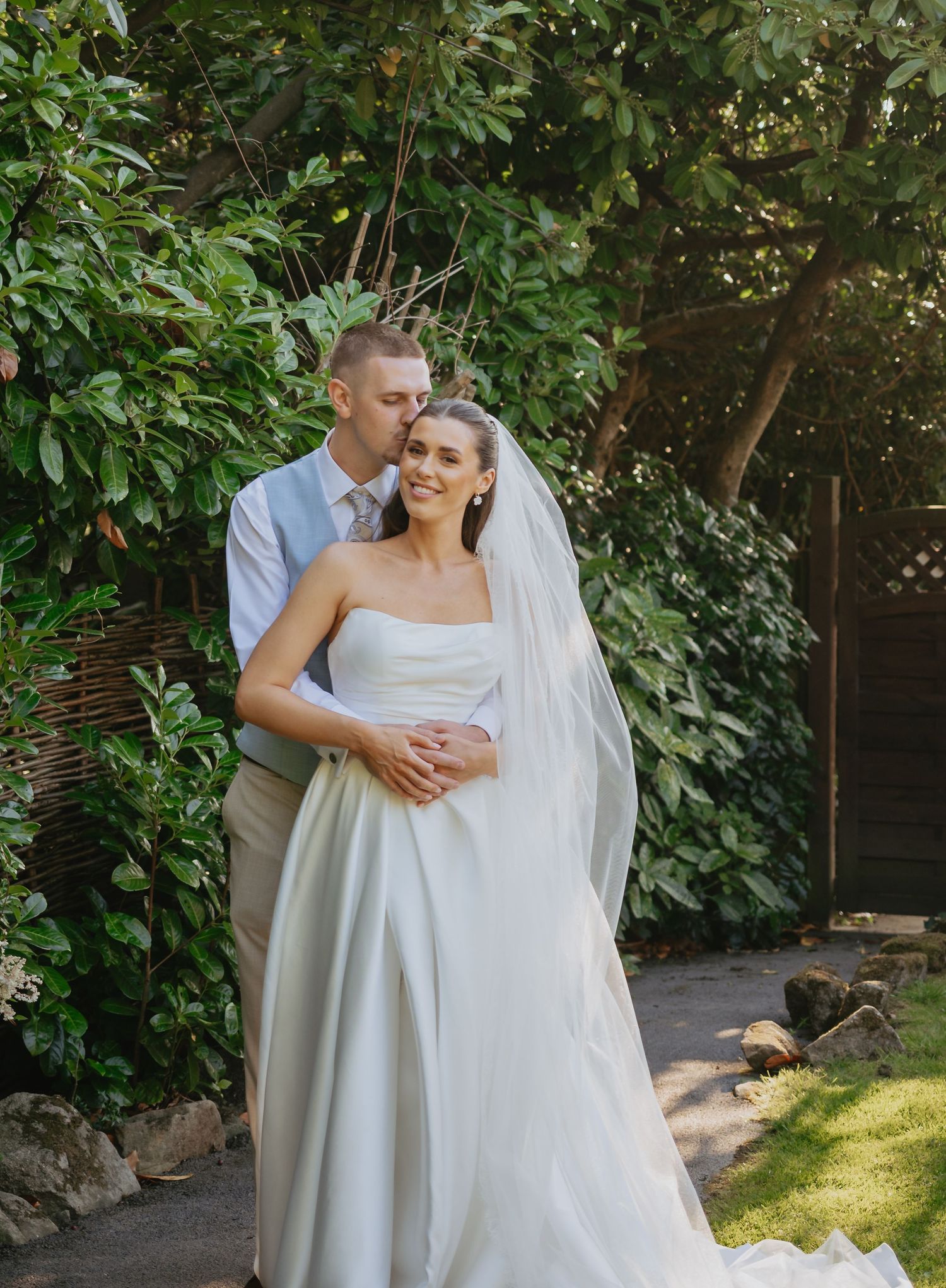 A romantic wedding moment captured in a garden setting with greenery and natural sunlight.