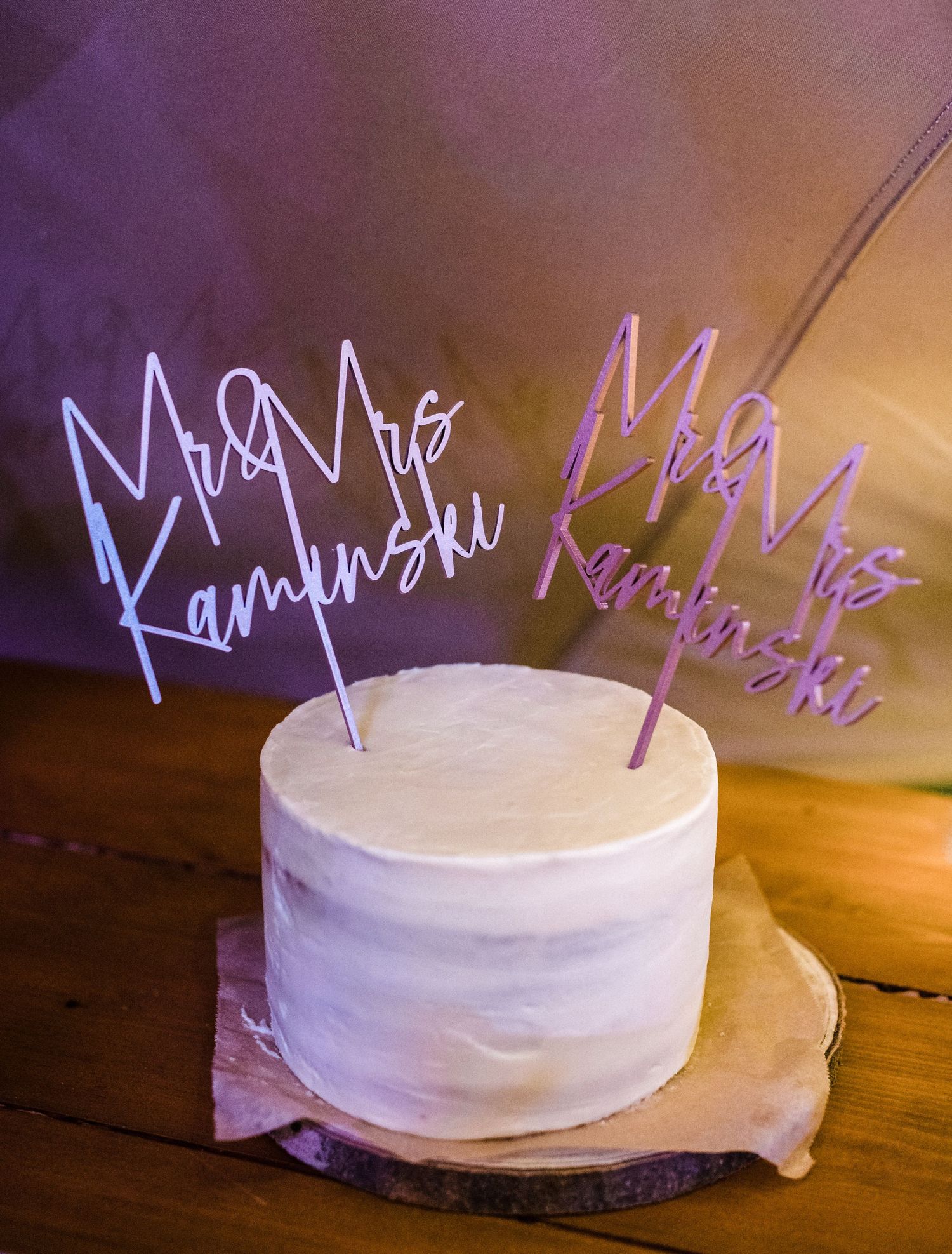 White wedding cake topped with glowing neon name signs in blue and pink.