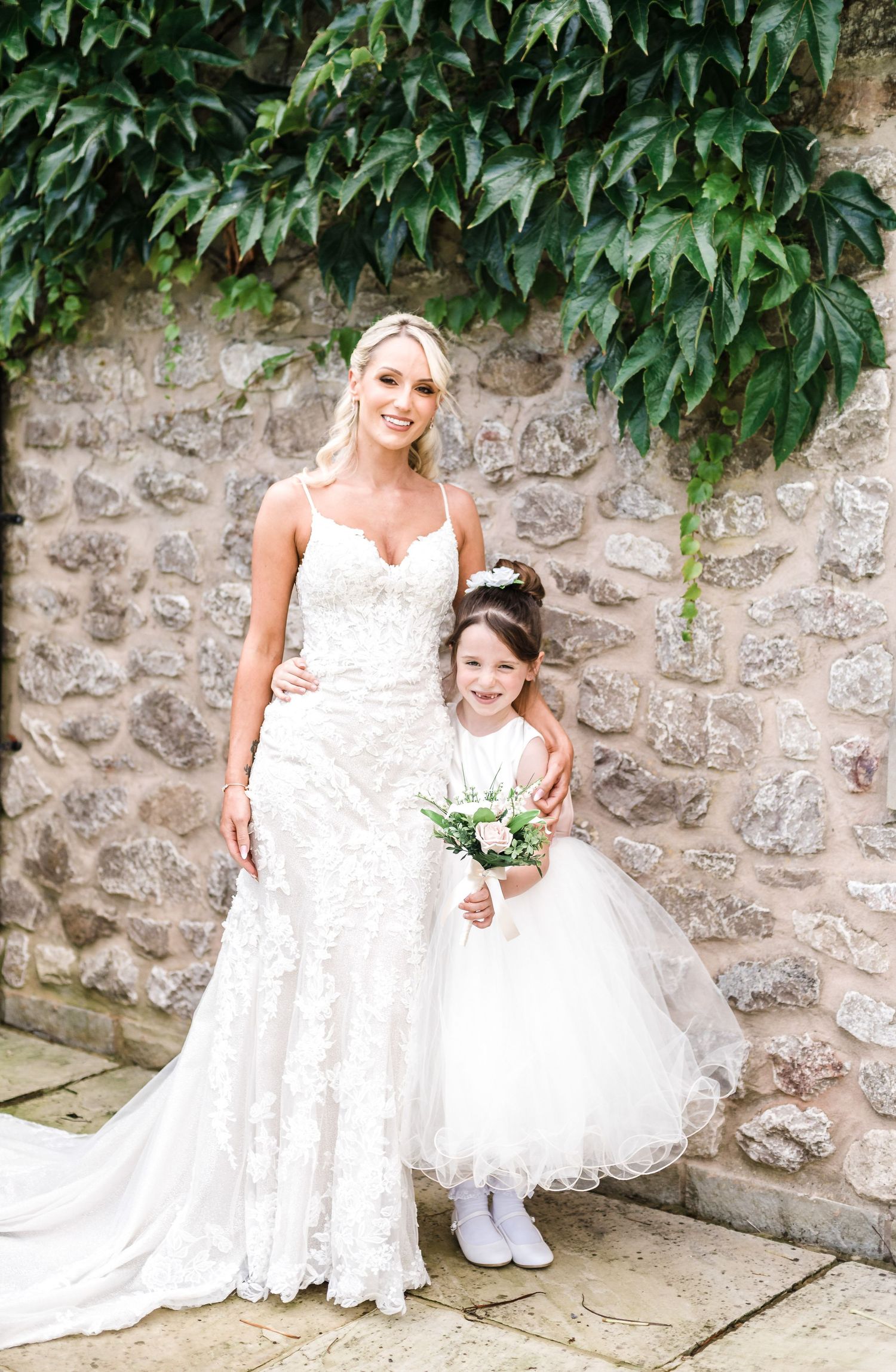 A sweet wedding moment captured against a stone wall with trailing vines.