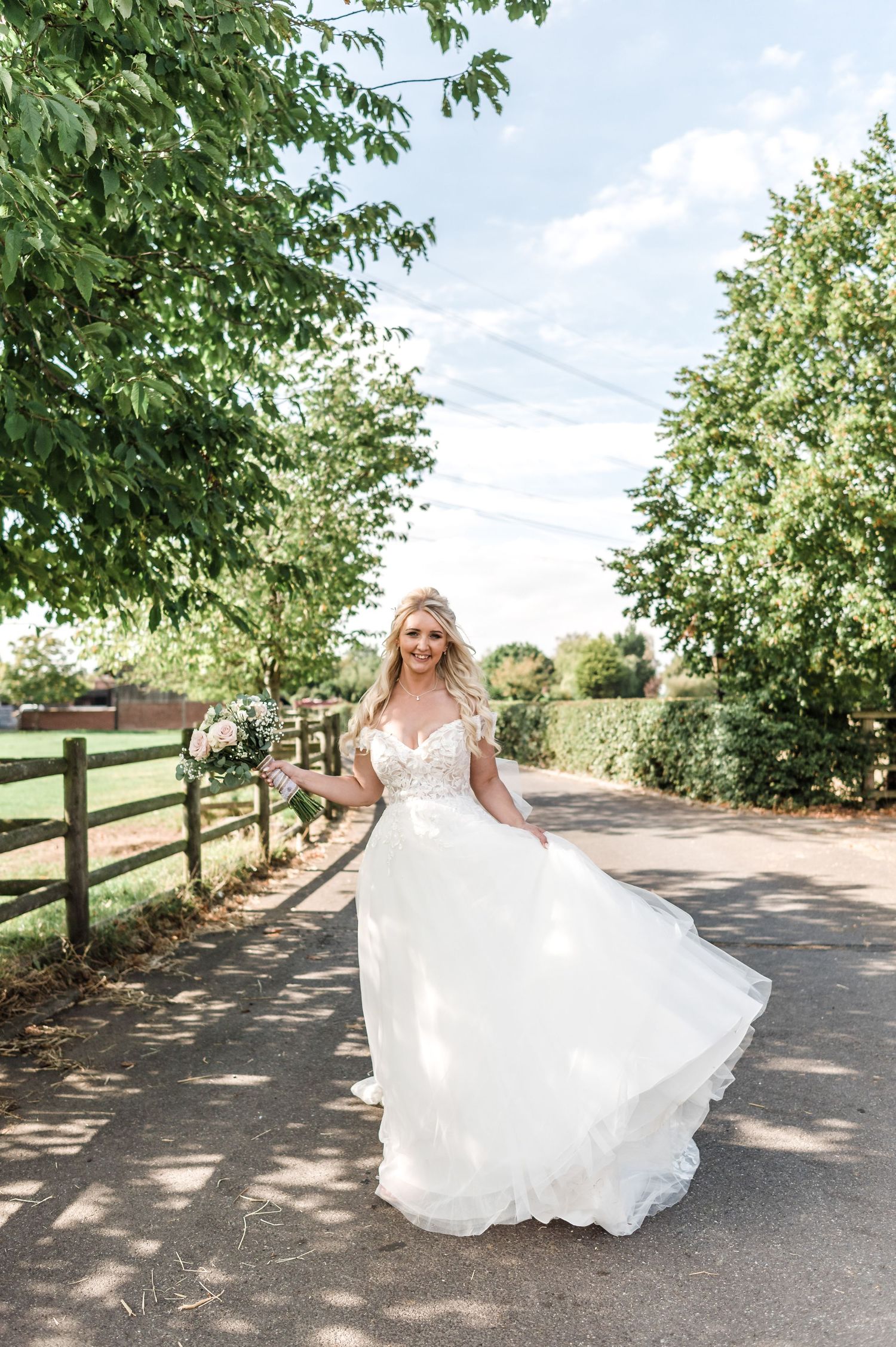 Bride twirls her flowing white dress on a tree-lined country path.