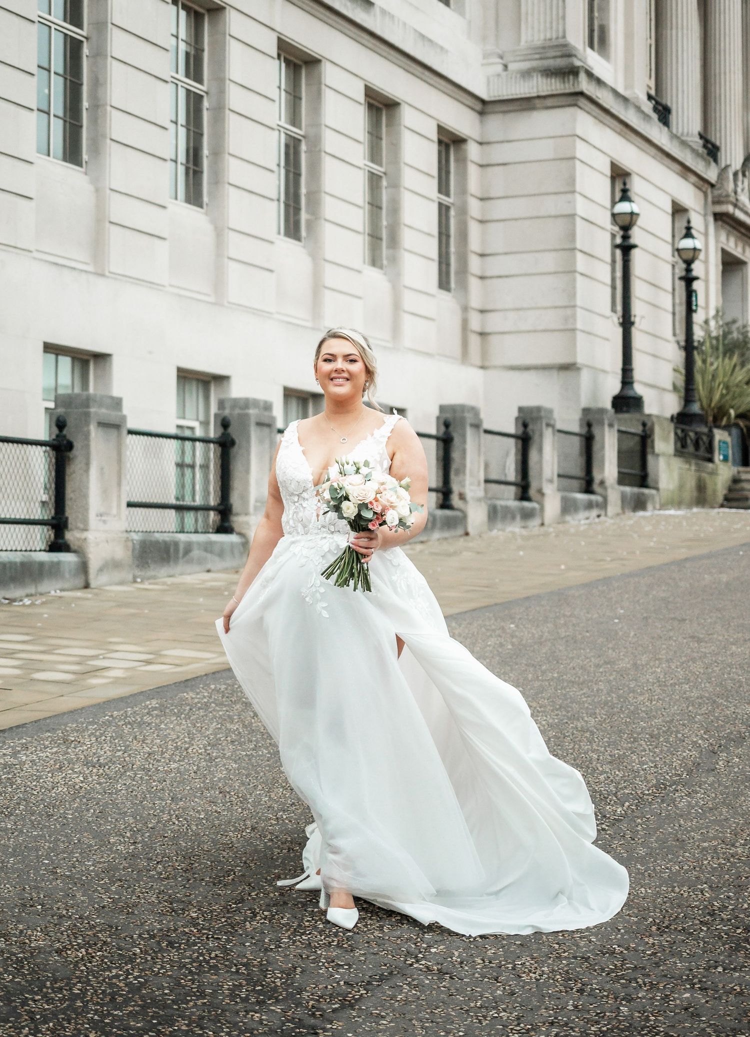 Elegant wedding portrait outside a grand classical building with flowing white dress catching the breeze.